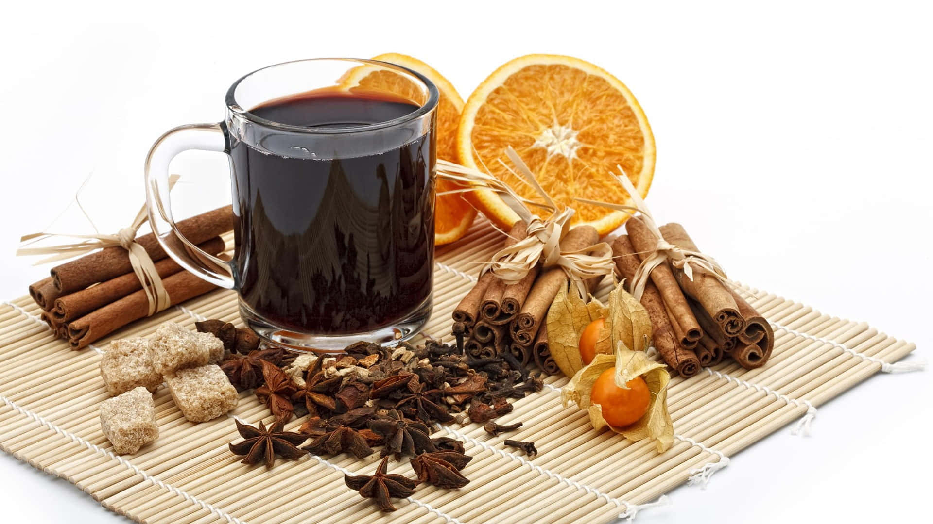 Mulled Wine 桌布 壁紙 — 一個玻璃杯裝的香料熱紅酒，周圍有肉桂棒、八角、方糖和橙片，放在竹墊上。