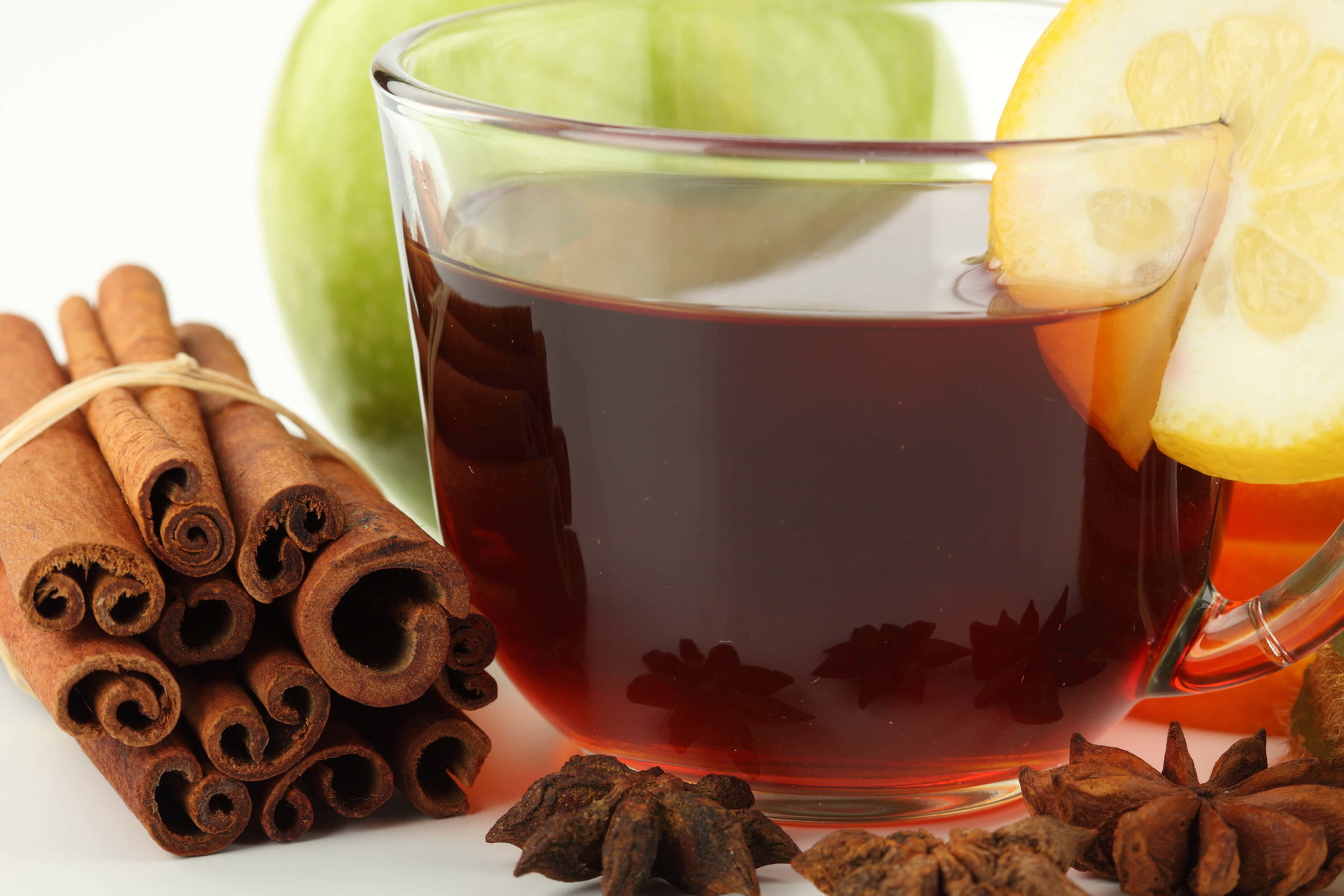 Mulled Wine 桌布 壁紙 — 一個玻璃杯裝著香料茶，配上檸檬片和八角，旁邊有肉桂棒和一個青蘋果，放在白色背景上。