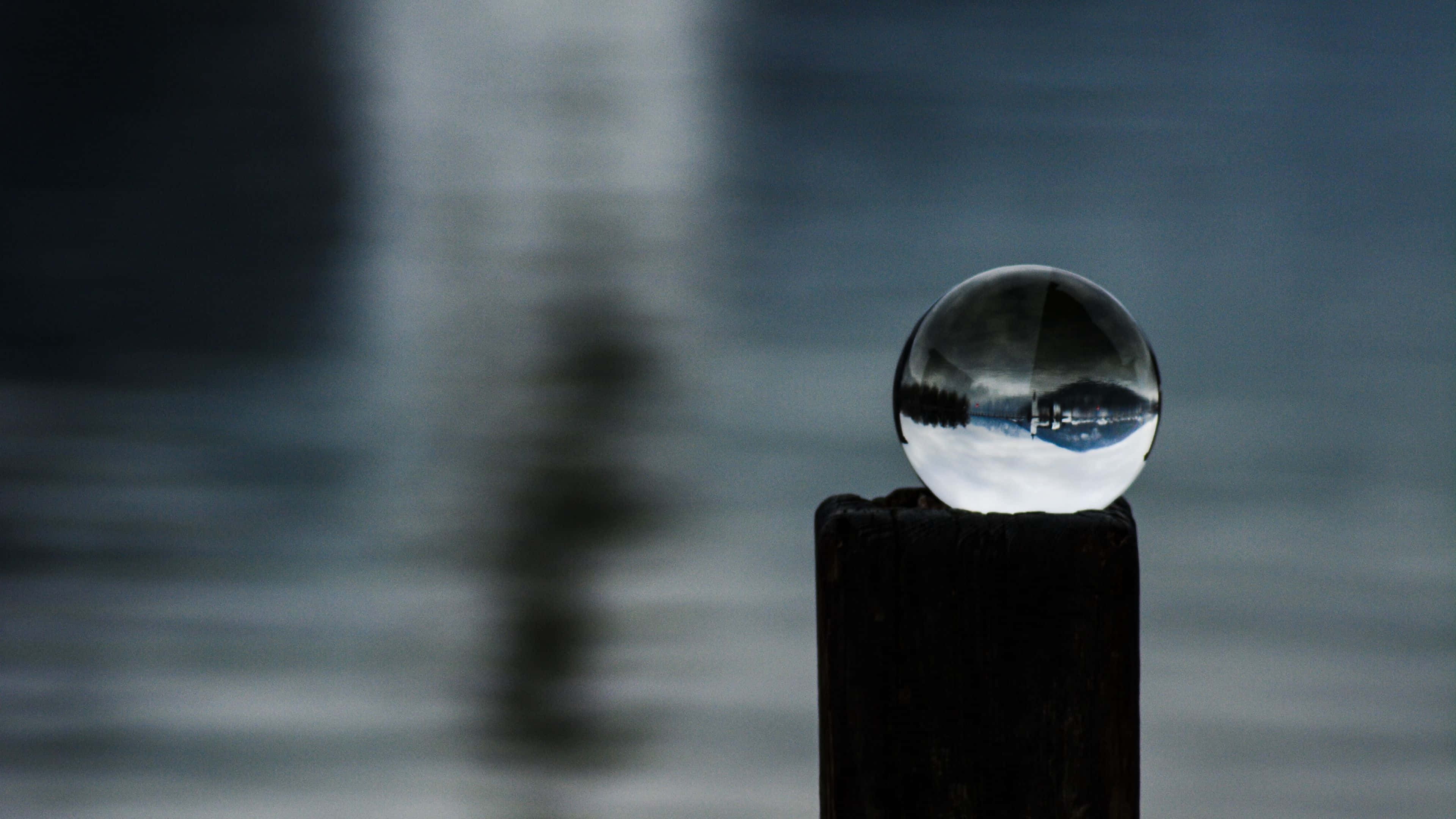 Crystal Ball 桌布 壁紙 — 一個玻璃球放在木柱上，映照出寧靜的湖泊和遠處的海岸線，背景是模糊的水面。