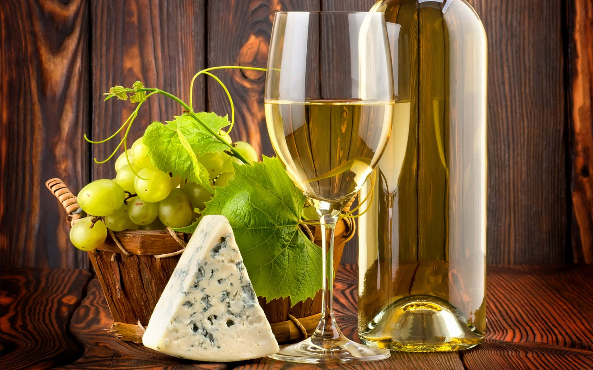 Food And Beverage 桌布 壁紙 — 一個玻璃瓶和一杯白酒放在一個裝有青葡萄的籃子和一塊藍紋起司旁邊，置於一張鄉村風格的木桌上。