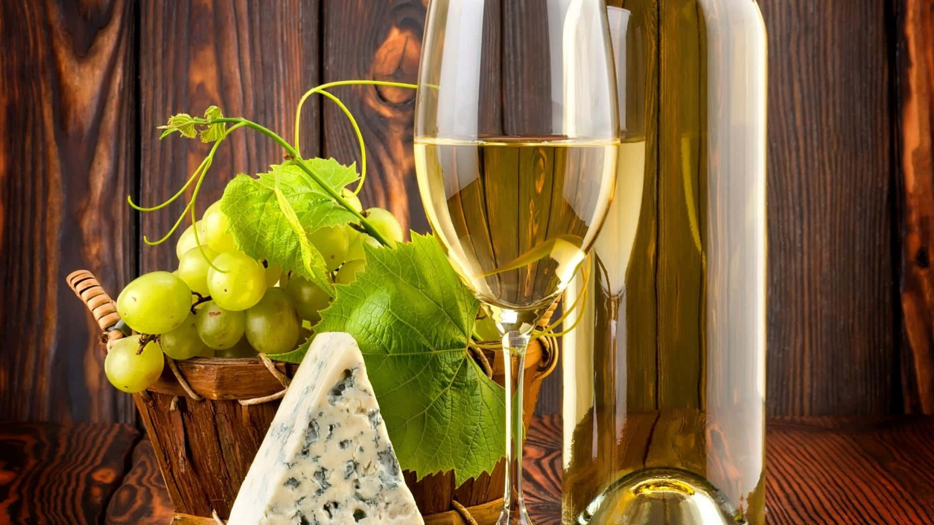 White Wine 桌布 壁紙 — 一個玻璃瓶和一杯白酒放在一個裝有青葡萄的籃子和一塊藍紋起司旁邊，放在一張質樸的木桌上。