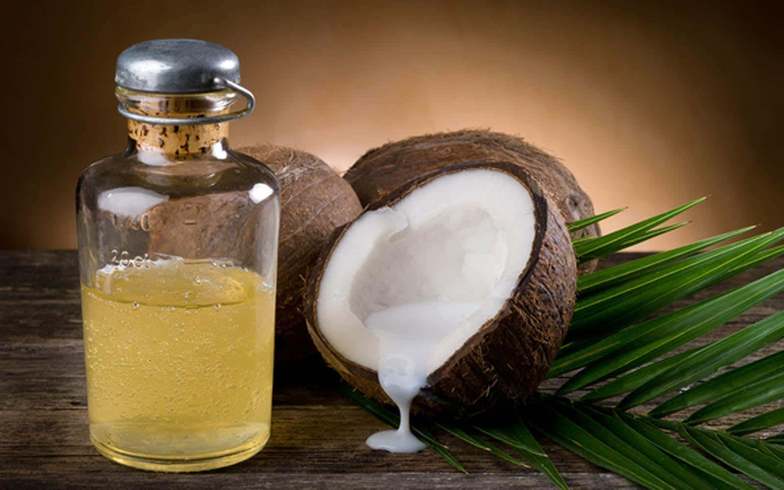 Coconut 桌布 壁紙 — 一個玻璃瓶的金色椰子油放在半個椰子旁邊，椰子滴下白色奶油到木質表面上的綠色棕櫚葉上。