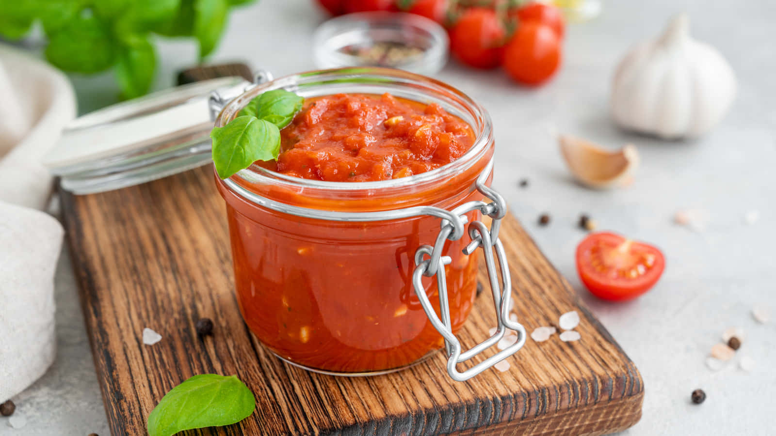 Red Sauce 桌布 壁紙 — 一個玻璃瓶裝滿鮮紅色自製番茄醬，放在木板上，周圍是新鮮羅勒、大蒜和櫻桃番茄。