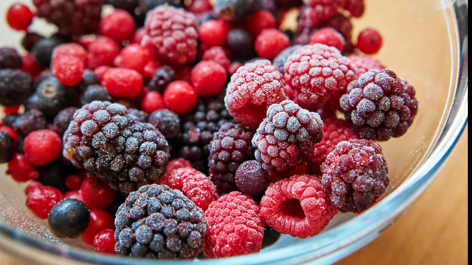Berry 桌布 壁紙 — 一個玻璃碗的特寫，裡面裝滿了鮮紅的覆盆子和深色藍莓，上面撒滿了霜。