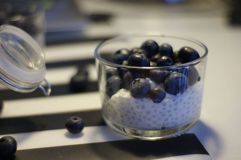 Blueberries 桌布 壁紙 — 一個玻璃碗裝滿了奶油白色的珍珠和新鮮藍莓，放在黑白條紋的表面上。