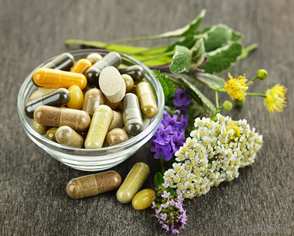 pills 桌布 壁紙 — 一個玻璃碗裝滿了彩色草藥膠囊和新鮮花朵，放在質樸的木質表面上。