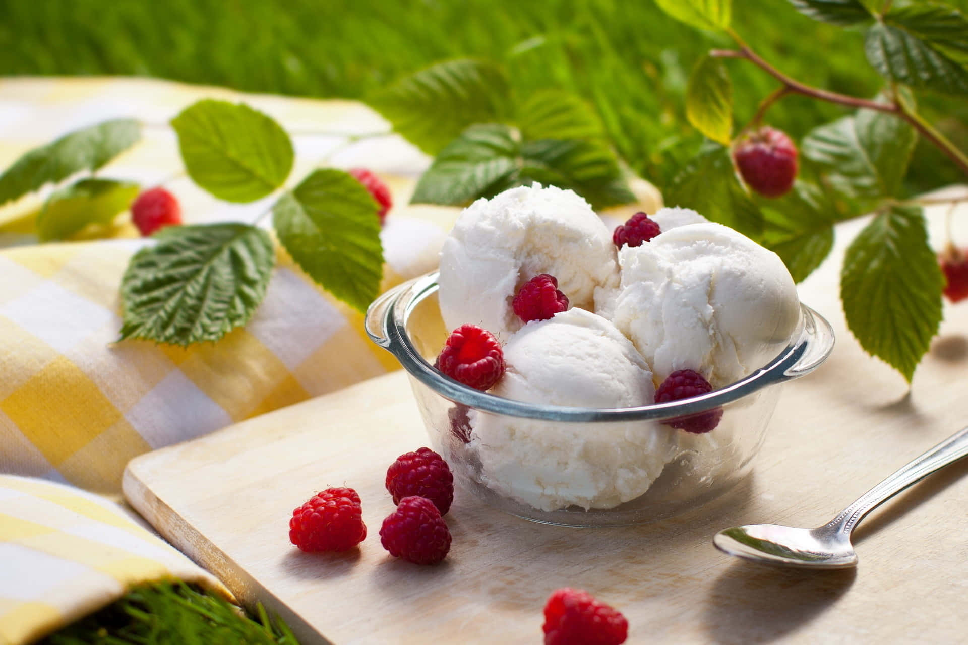Raspberry 桌布 壁紙 — 一個玻璃碗裝著奶油香草冰淇淋，上面放上新鮮覆盆子，放在木板上，旁邊有黃色格子布和綠色植物。