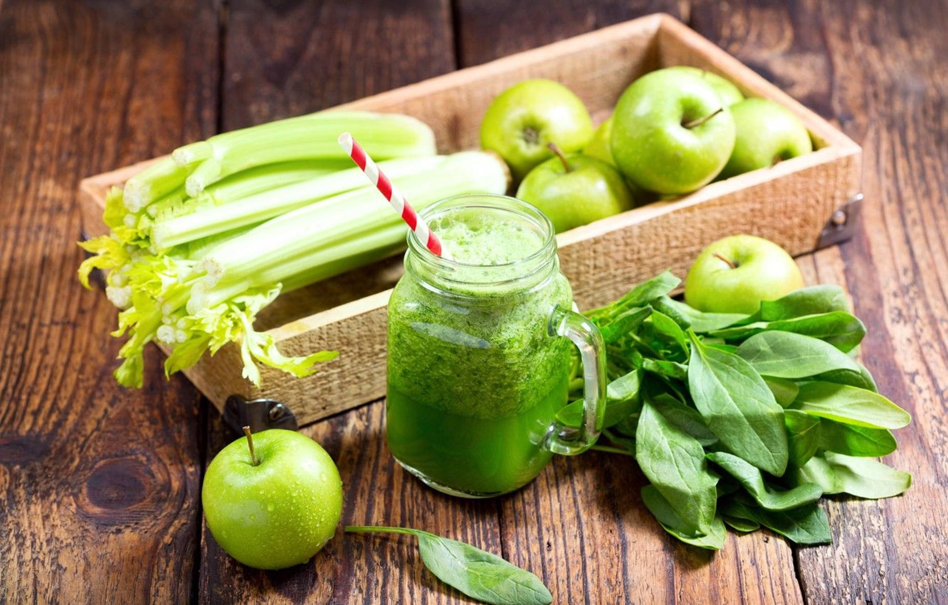 Healthy Food 桌布 壁紙 — 一個玻璃罐中的鮮豔綠色冰沙，旁邊放著新鮮菠菜、芹菜和青蘋果，置於質樸的木桌上。