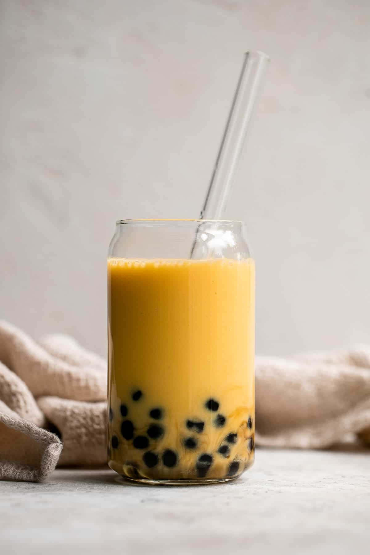 Boba Tea 桌布 壁紙 — 一個玻璃罐中的鮮黃色珍珠奶茶，配有黑色木薯珍珠和透明吸管，背景是柔軟的米色布料。
