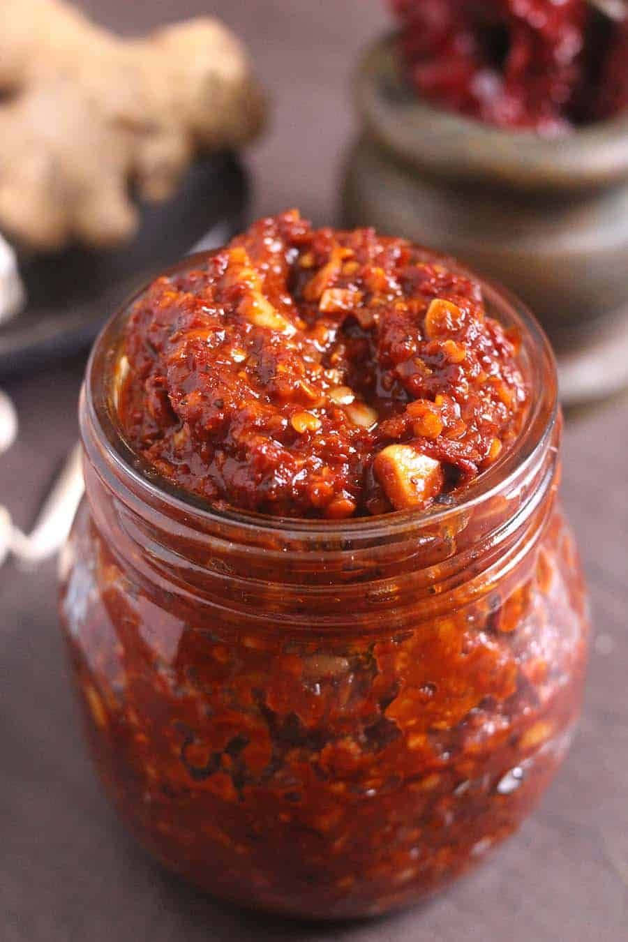 Szechuan Sauce 桌布 壁紙 — 一個玻璃罐的特寫，裡面裝滿了粗粒紅辣椒醬，可見蒜頭和生薑塊。
