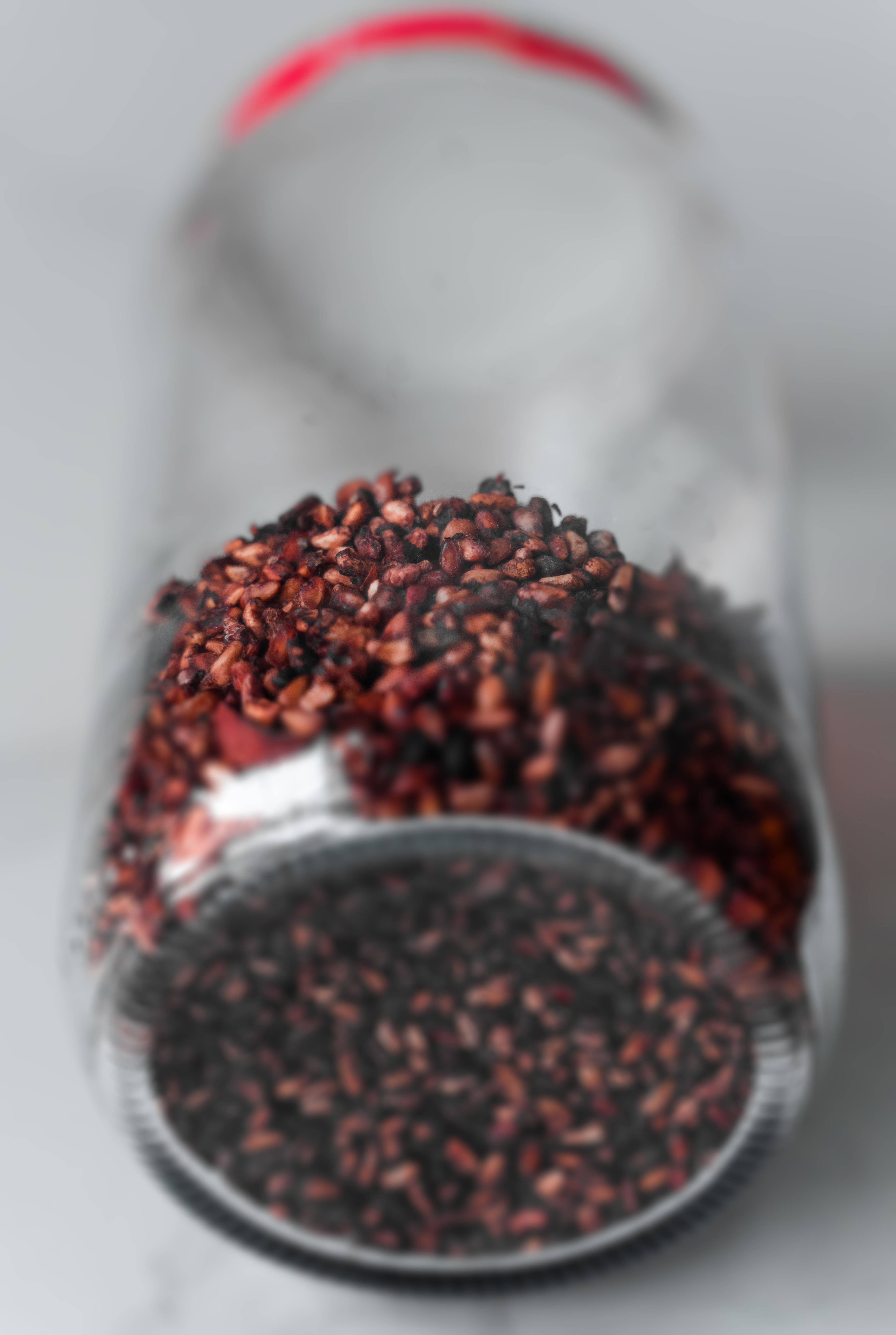 4K 桌布 壁紙 — 一個玻璃罐的特寫，裡面裝滿深紅色和黑色的種子，側躺著，背景是柔和的白色。