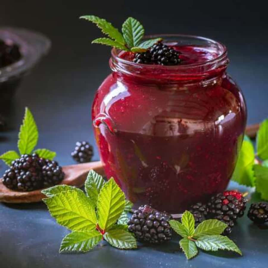 Blackberry Jam 桌布 壁紙 — 一個玻璃罐裝滿了閃亮的黑莓果醬，上面放著新鮮的莓果和薄荷葉，放在深色石板表面上。