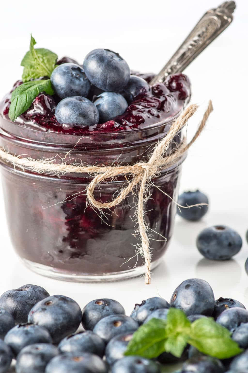 Blueberry Jam 桌布 壁紙 — 一個玻璃罐裝滿濃郁的深色藍莓果醬，上面放上新鮮藍莓和薄荷葉，並用麻繩綁好。