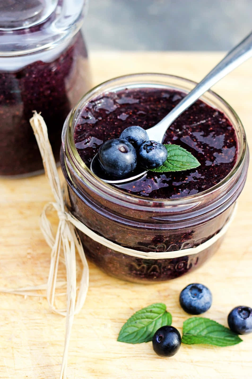 Blueberry Jam 桌布 壁紙 — 一個玻璃罐裝滿濃郁的深藍莓果醬，上面放上新鮮莓果和薄荷葉，置於木質表面上。