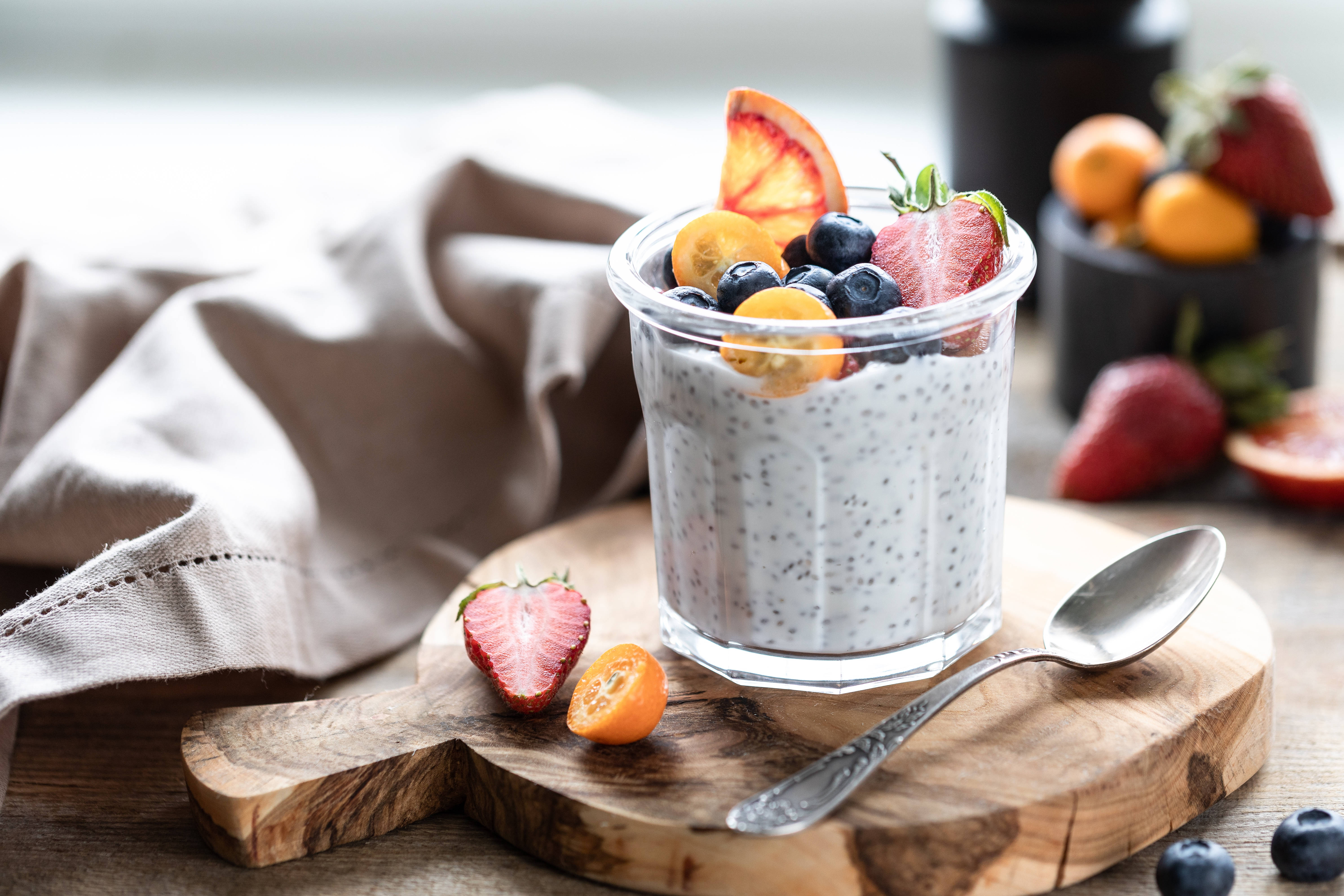 Yogurt 桌布 壁紙 — 一個玻璃罐裝的奇亞籽布丁，上面放著新鮮莓果和柑橘片，放在一個質樸的木板上，旁邊有一把湯匙。
