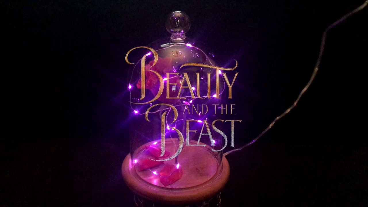 beast 桌布 壁紙 — 一個玻璃罩內有發光的紫色仙女燈，將標題 Beauty and the Beast 以優雅的金色字體包裹在深色背景上。