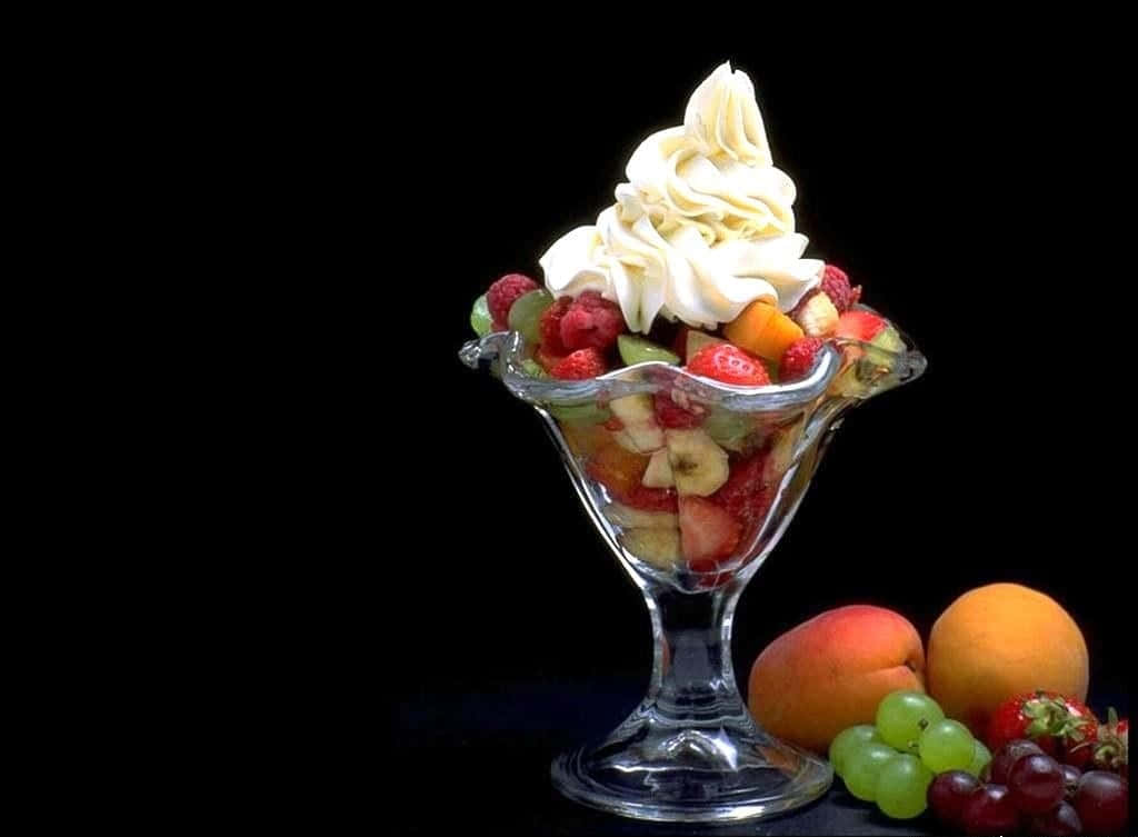 Ice Cream 桌布 壁紙 — 一個玻璃聖代碗，盛滿色彩繽紛的新鮮水果，上面有漩渦狀的奶油鮮奶油，襯托在純黑背景上。