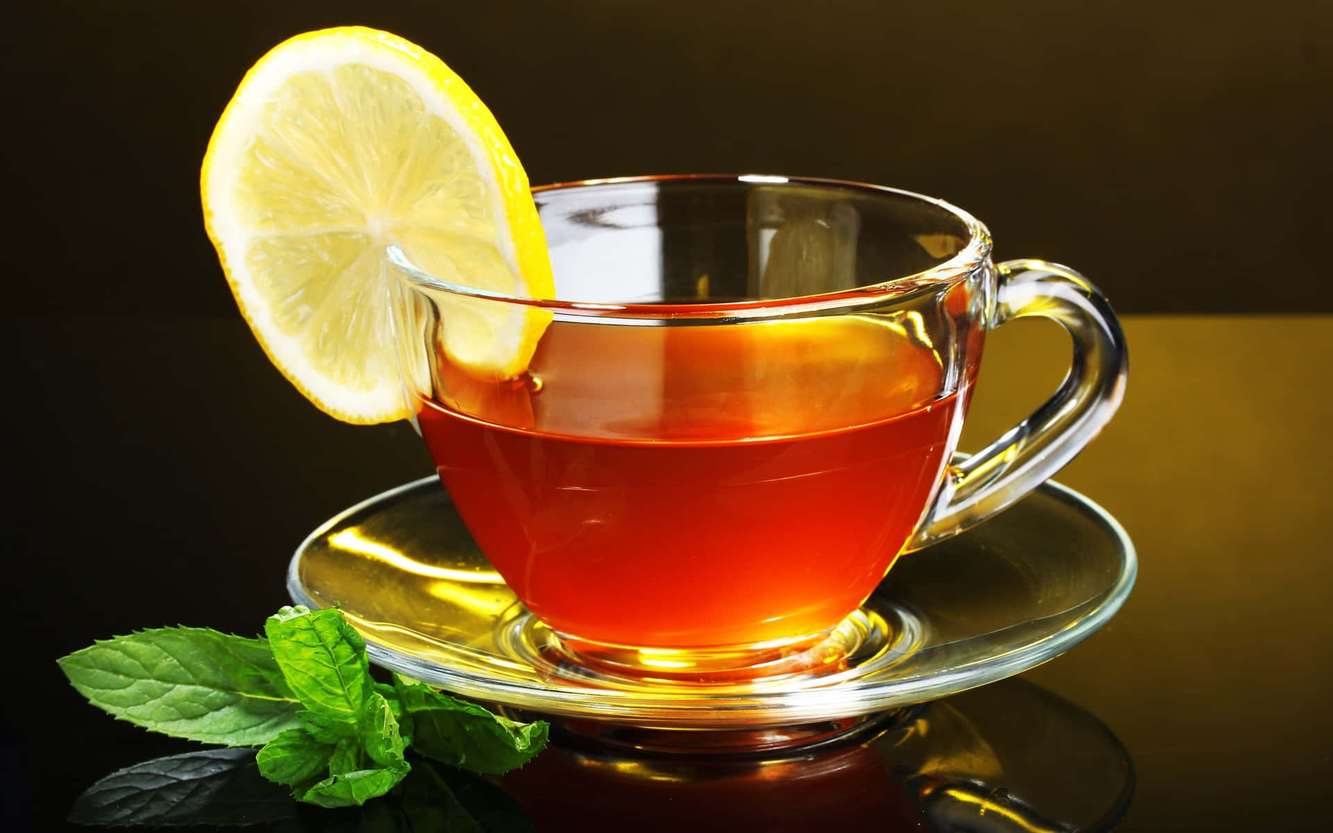咖啡動圖 桌布 壁紙 — 一個玻璃茶杯，裝滿琥珀色茶和一片檸檬，放在碟子上，旁邊是新鮮薄荷葉，背景為深色。