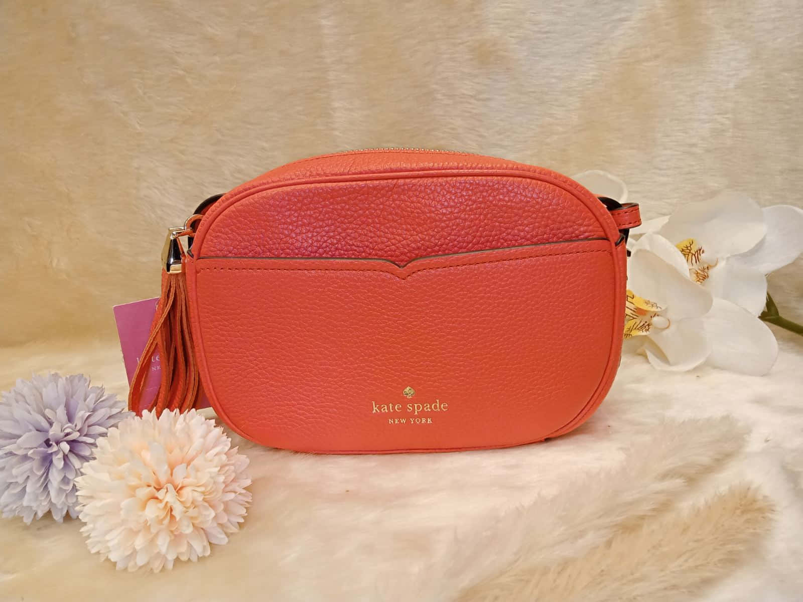 kate spade 桌布 壁紙 — 一個珊瑚色kate spade斜背包放在蓬鬆的米色毛皮上，旁邊有白色蘭花和粉彩絨球。