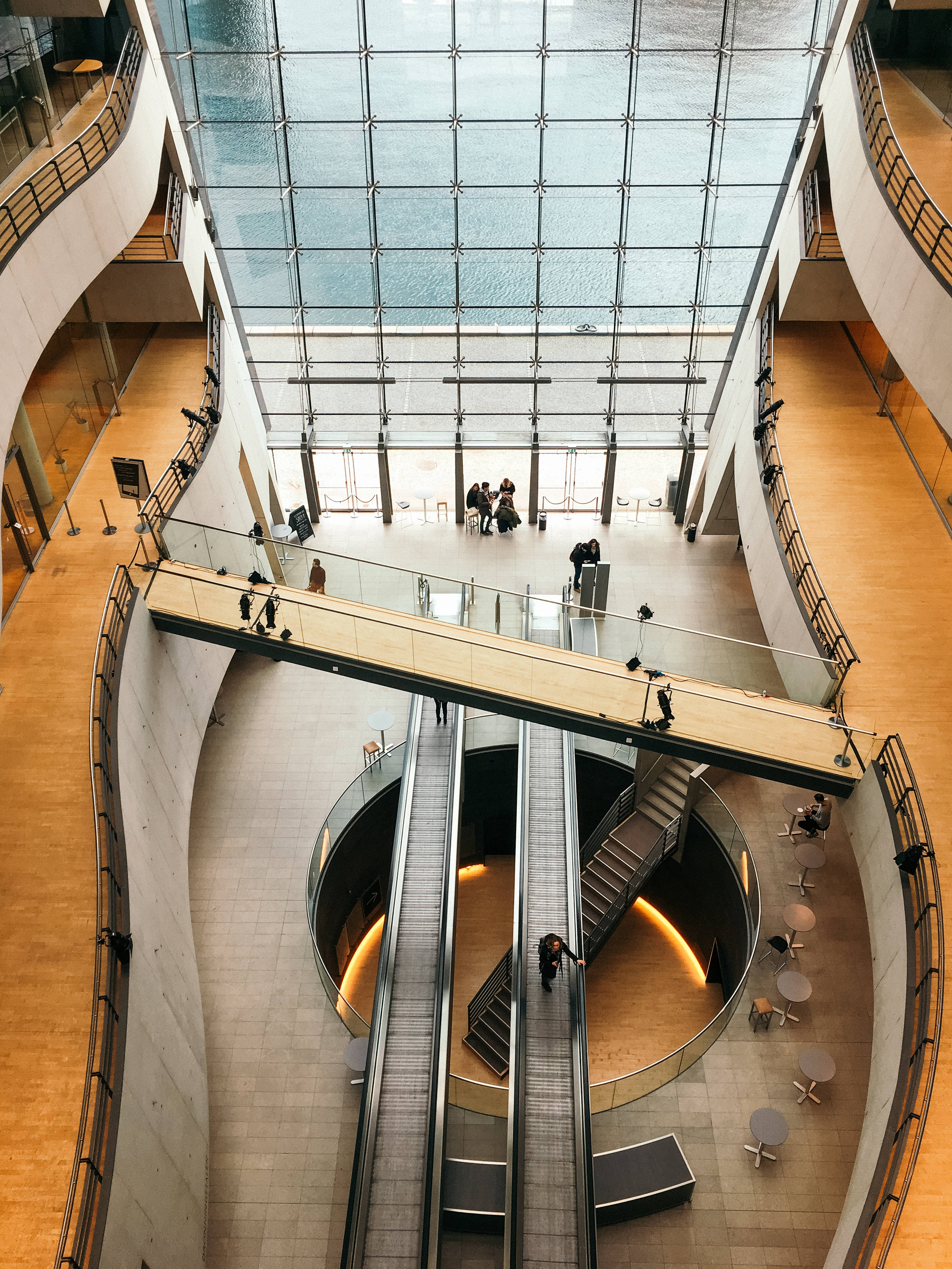Denmark 桌布 壁紙 — 一個現代中庭，設有弧形電扶梯和玻璃走道，上方是廣闊的天窗，人們在其中穿梭。