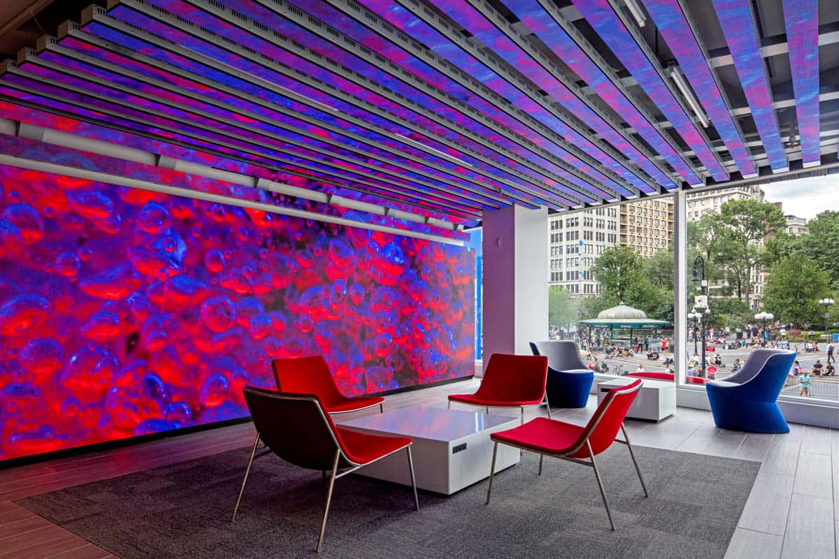 Interior Design 桌布 壁紙 — 一個現代休息室，配有鮮明的紅色椅子和充滿活力的紅藍數位牆，位於條紋天花板下，俯瞰城市公園。
