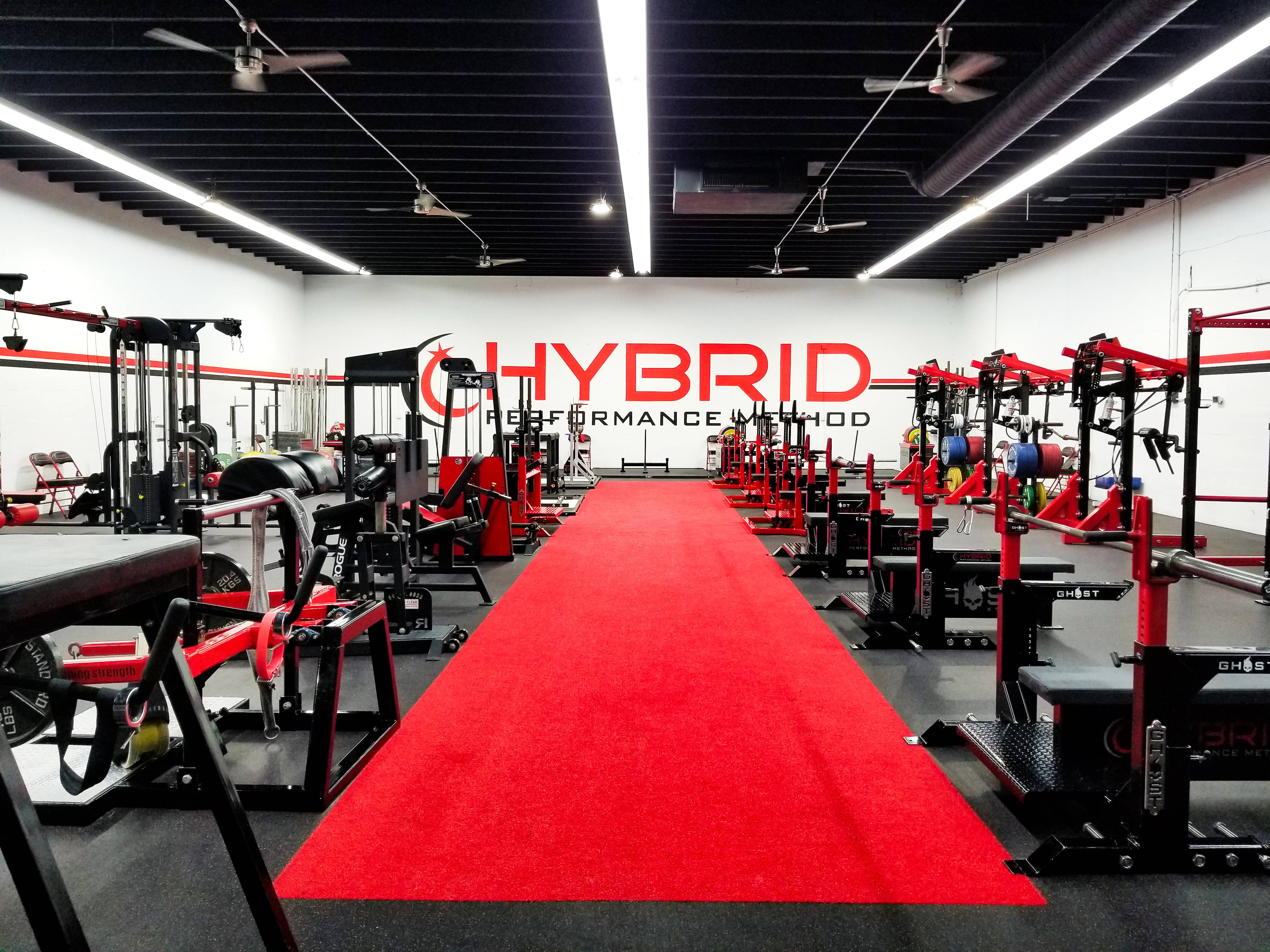 Weightlifting 桌布 壁紙 — 一個現代化的健身房，紅色地毯走廊兩旁擺放著黑色和紅色的舉重器材，上方是明亮的螢光燈。