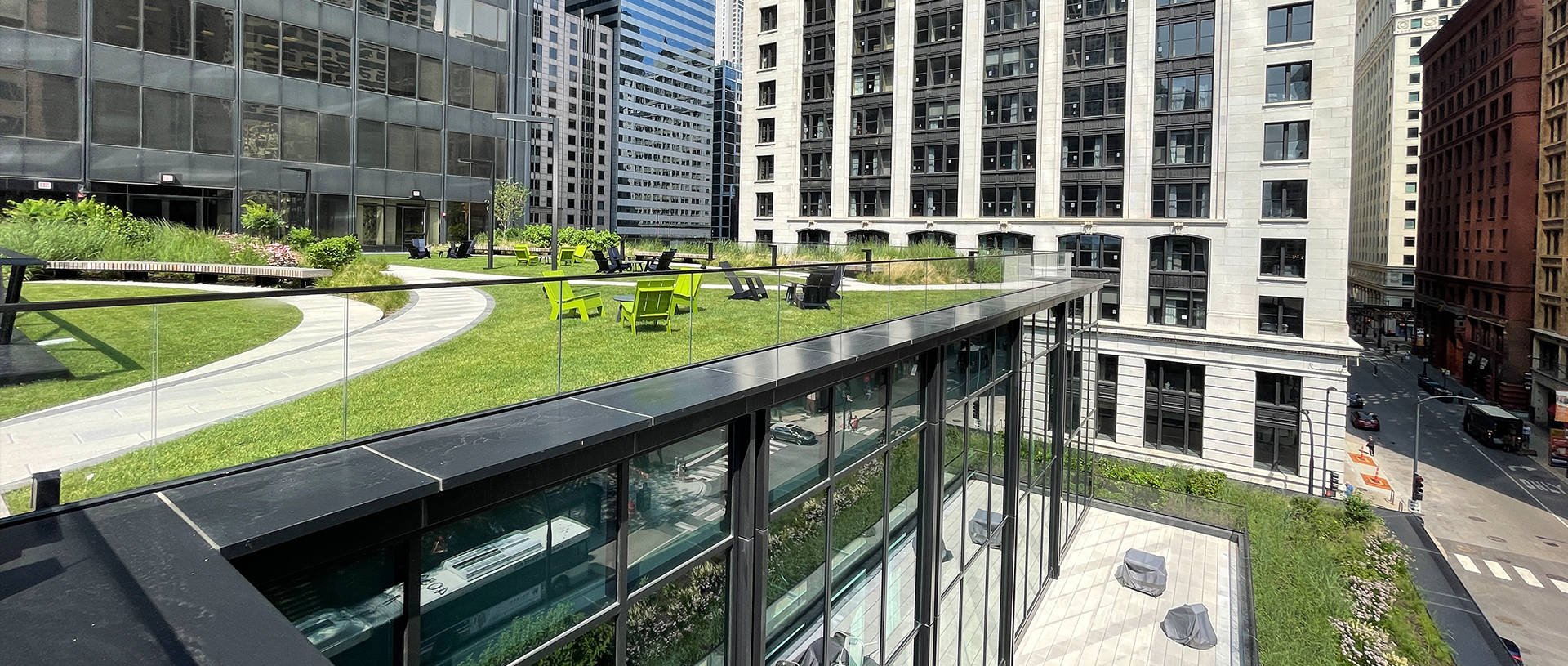 Buildings 桌布 壁紙 — 一個現代化的屋頂花園，有蜿蜒的小徑、綠草和鮮黃色的椅子，周圍是高樓大廈，在晴朗的日光下。