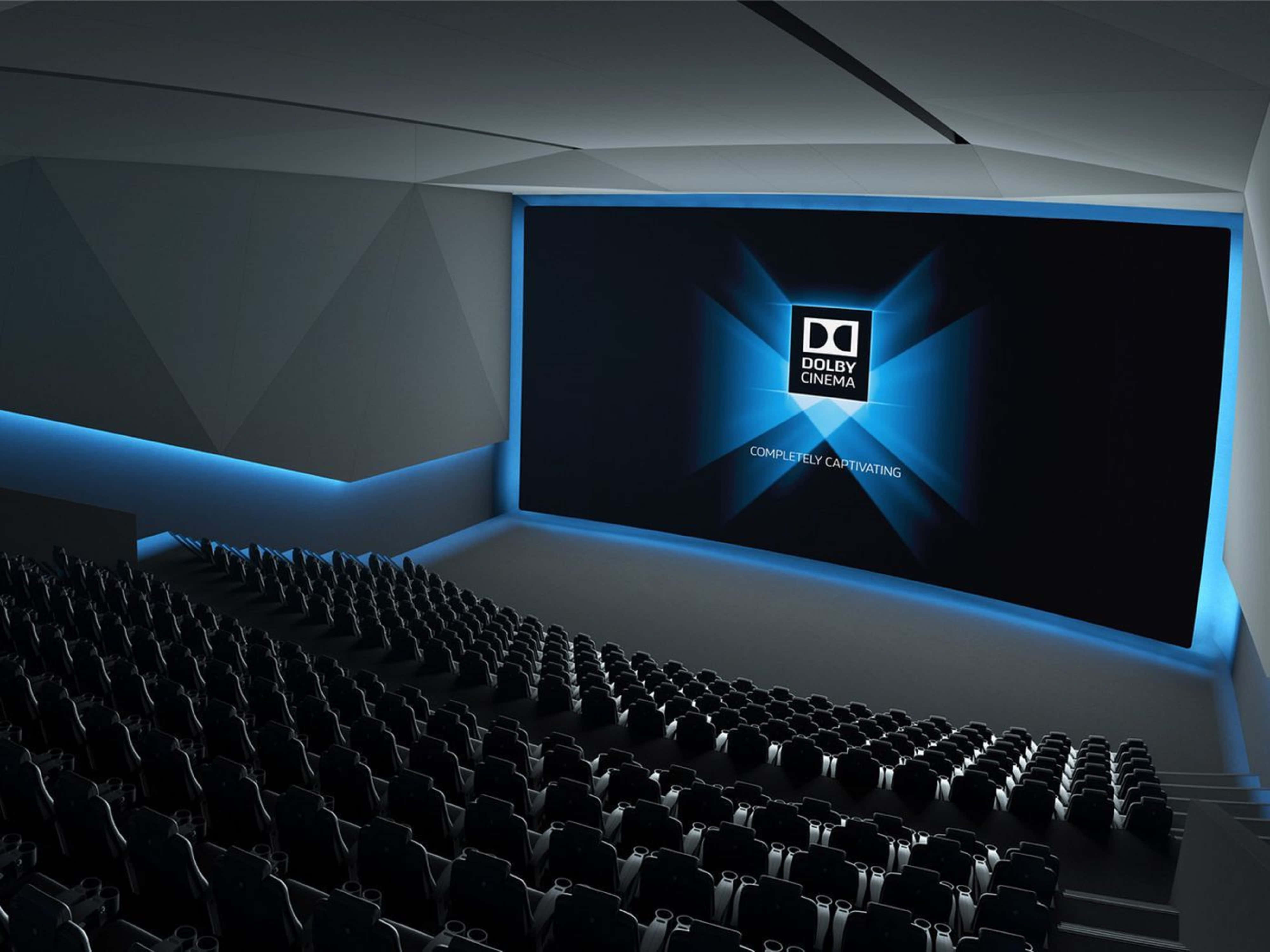 4K Dolby Vision 桌布 壁紙 — 一個現代化的電影院禮堂，排列著黑色座椅，面向一個顯示Dolby Cinema標誌並被藍光照亮的大螢幕。