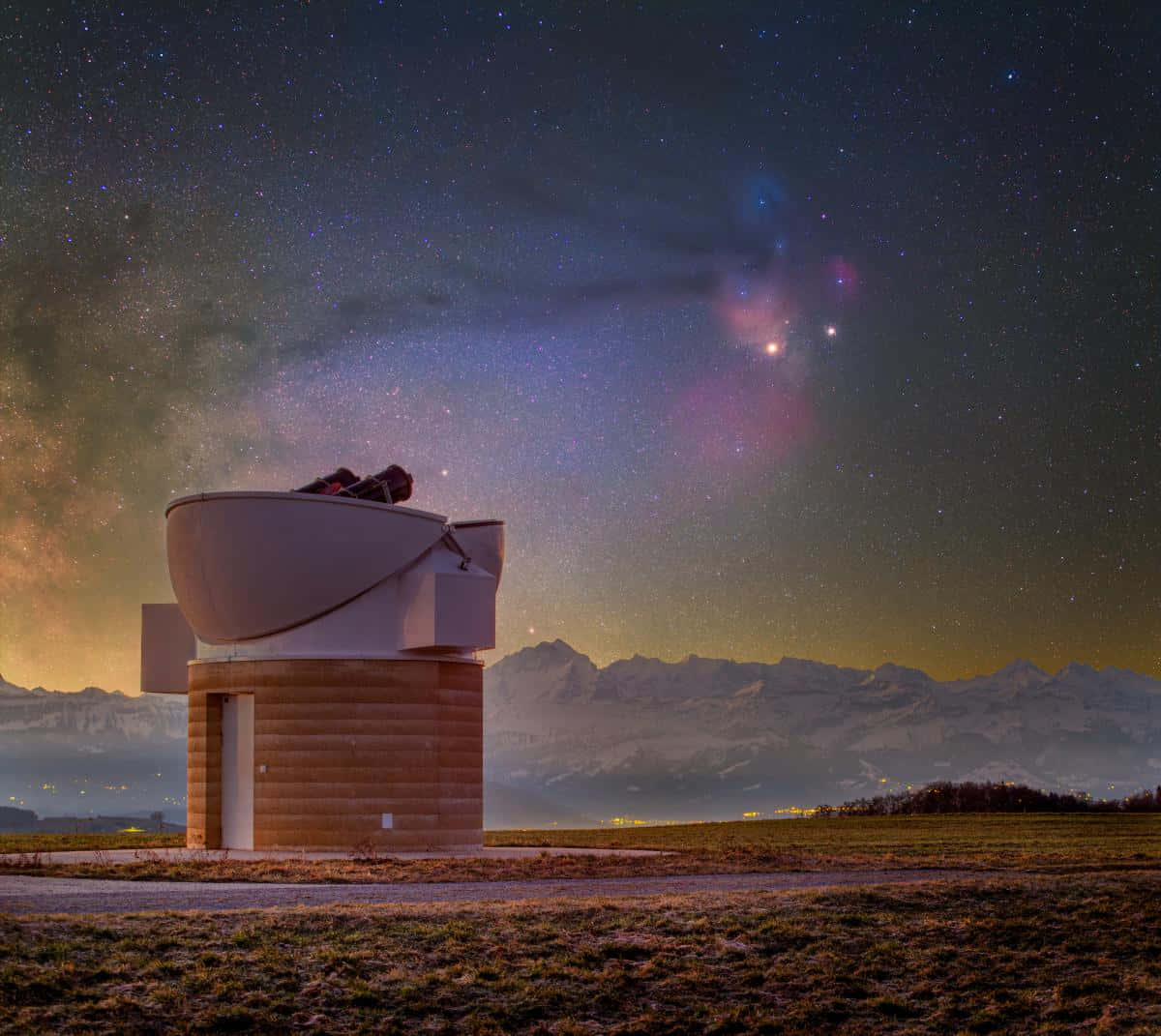 astronomy 桌布 壁紙 — 一個現代天文台獨自矗立在繁星點點的夜空下，下方有鮮豔的星雲和遠處白雪覆蓋的山脈微微發光。