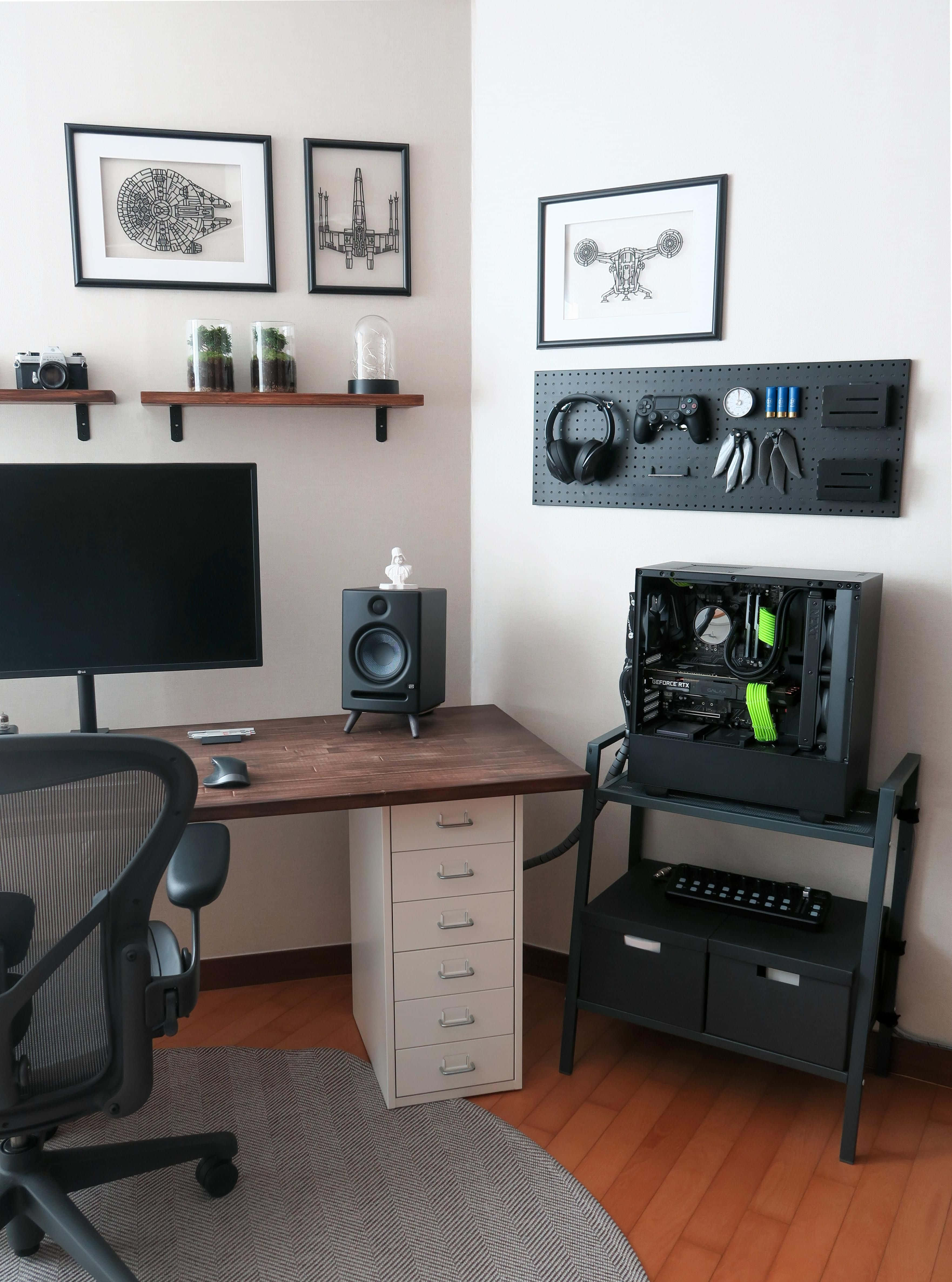 Gaming Accessories 桌布 壁紙 — 一個現代家居辦公室，配有木桌、黑色電競椅和金屬支架上的開放式PC機殼，周圍環繞著裱框的星際大戰藝術品和浮動層架。