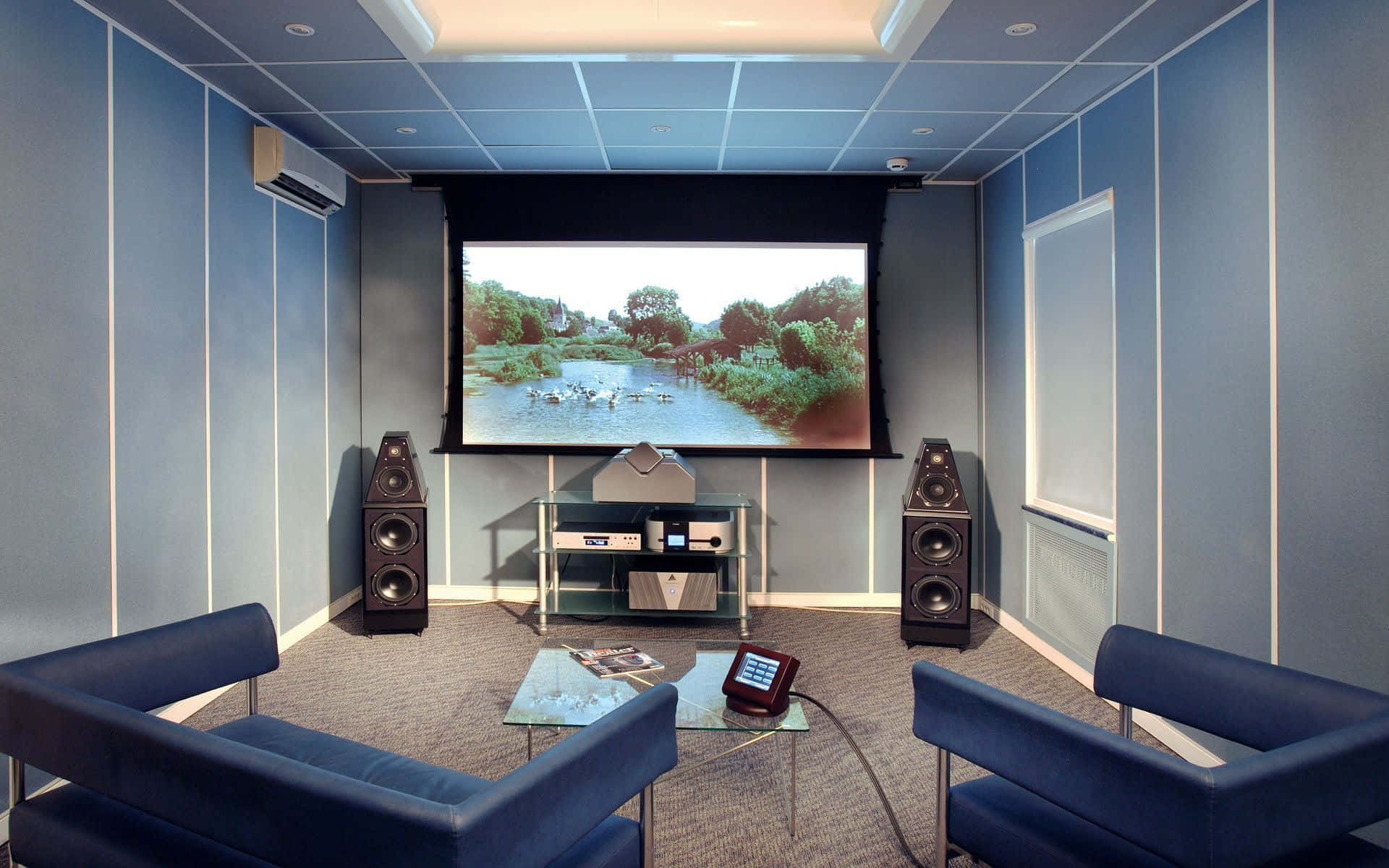 Home Cinema 桌布 壁紙 — 一個現代家庭影院房間，藍色牆壁和椅子面向一個大屏幕，顯示寧靜的河流場景和鴨子。