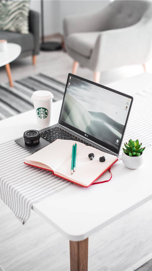 MacBook 動態圖片 桌布 壁紙 — 一個現代工作空間，在簡約風格的客廳中，白色桌子上放有筆記型電腦、筆記本、咖啡和多肉植物。