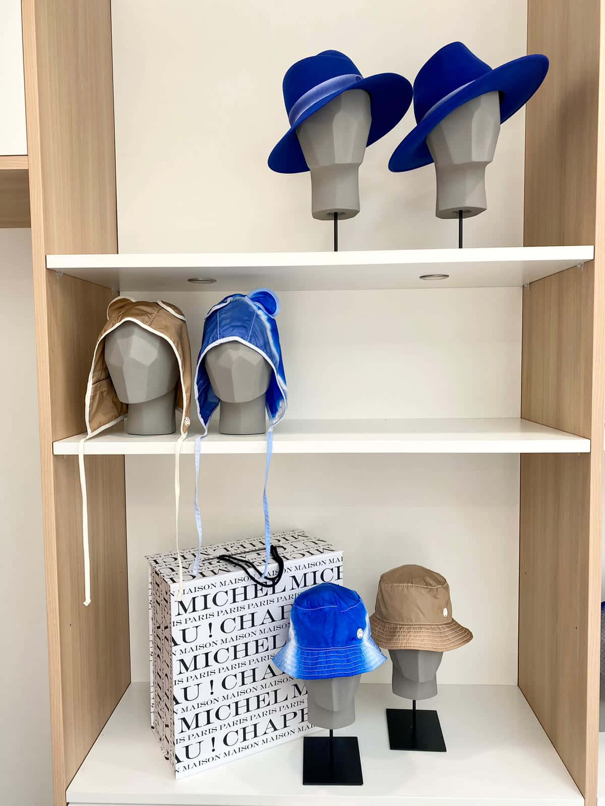 Clothes 桌布 壁紙 — 一個現代木架展示多種帽子戴在人體模型頭上，下方有一個品牌購物袋。