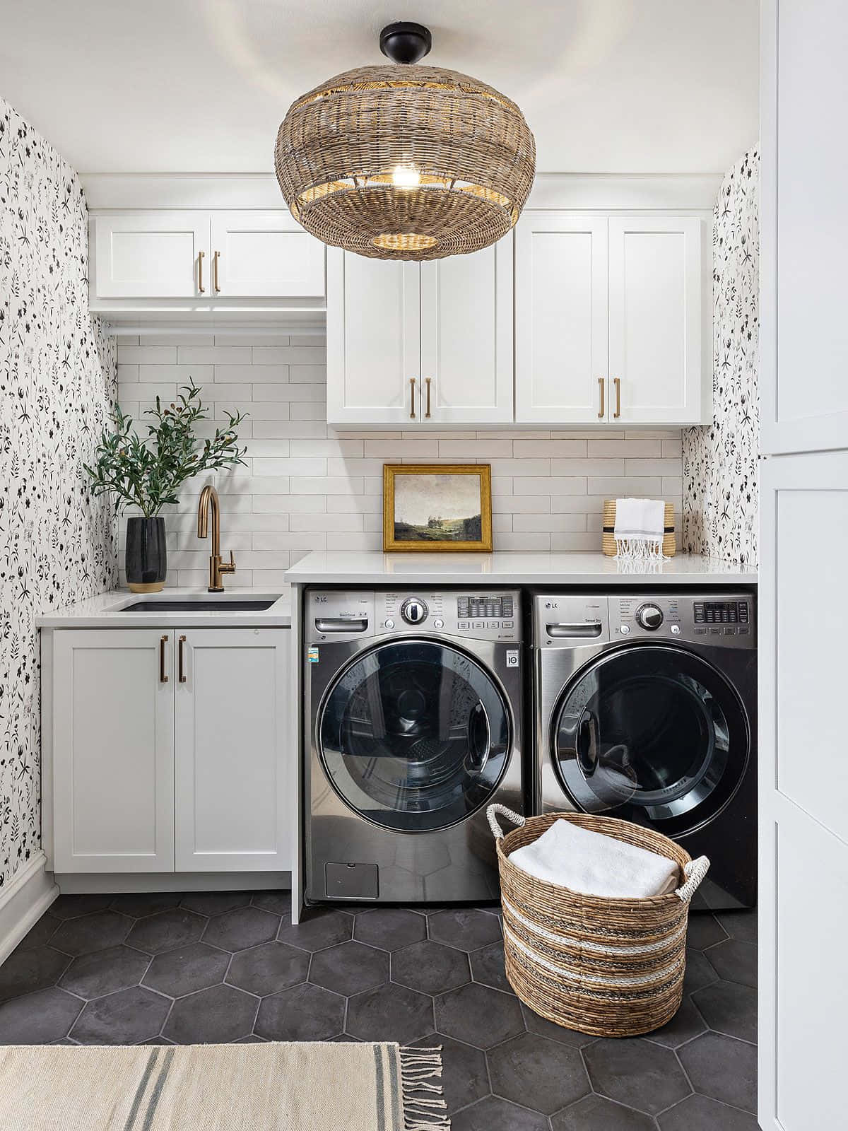washing machine 桌布 壁紙 — 一個現代洗衣房，配有白色櫥櫃、六角形深灰色地磚，以及兩部不鏽鋼前置式洗衣機上方的編織吊燈。