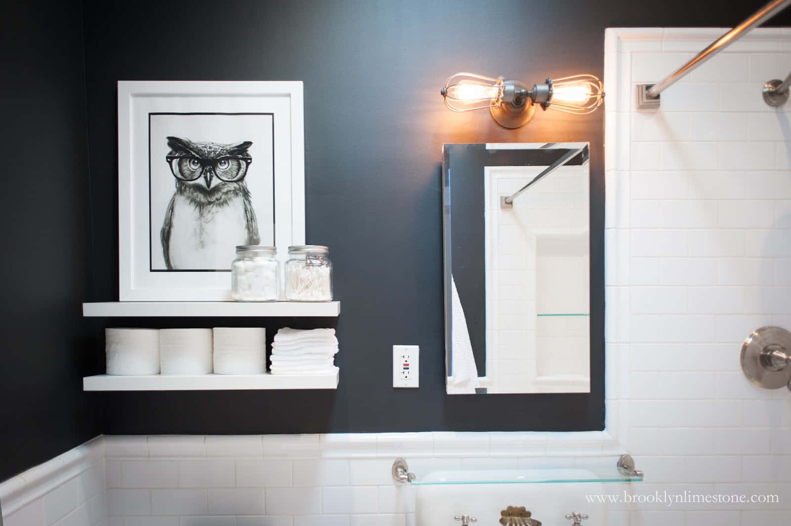 Black And White Bathroom 桌布 壁紙 — 一個現代浴室，深色牆壁，配有框裝貓頭鷹藝術品和復古風格燈具，位於白色瓷磚淋浴間上方。