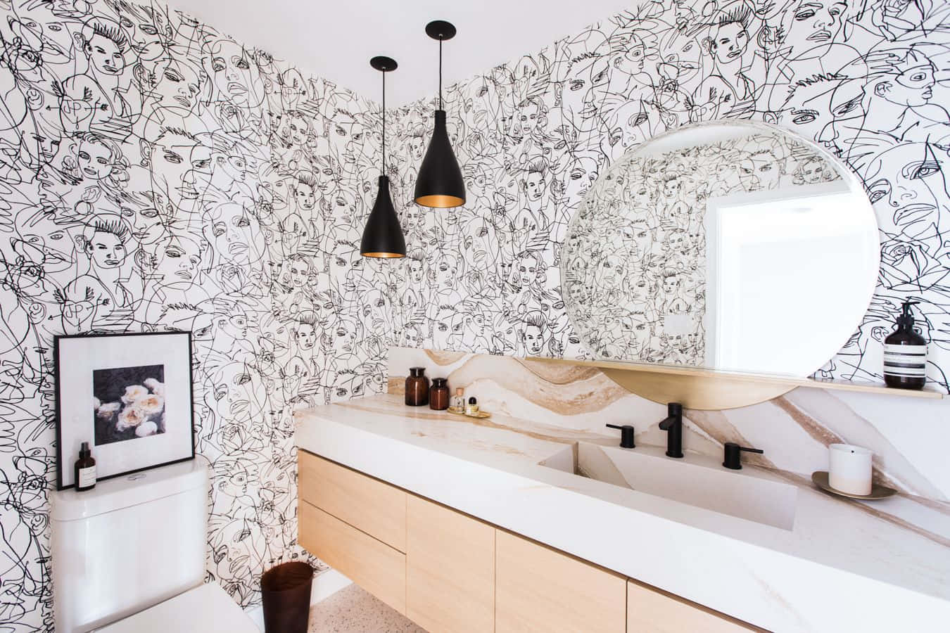 Bathroom Decor 桌布 壁紙 — 一個現代浴室，牆上覆蓋著黑白線條繪製的臉孔，木製洗手台上方有一個圓形鏡子，配有黑色配件。