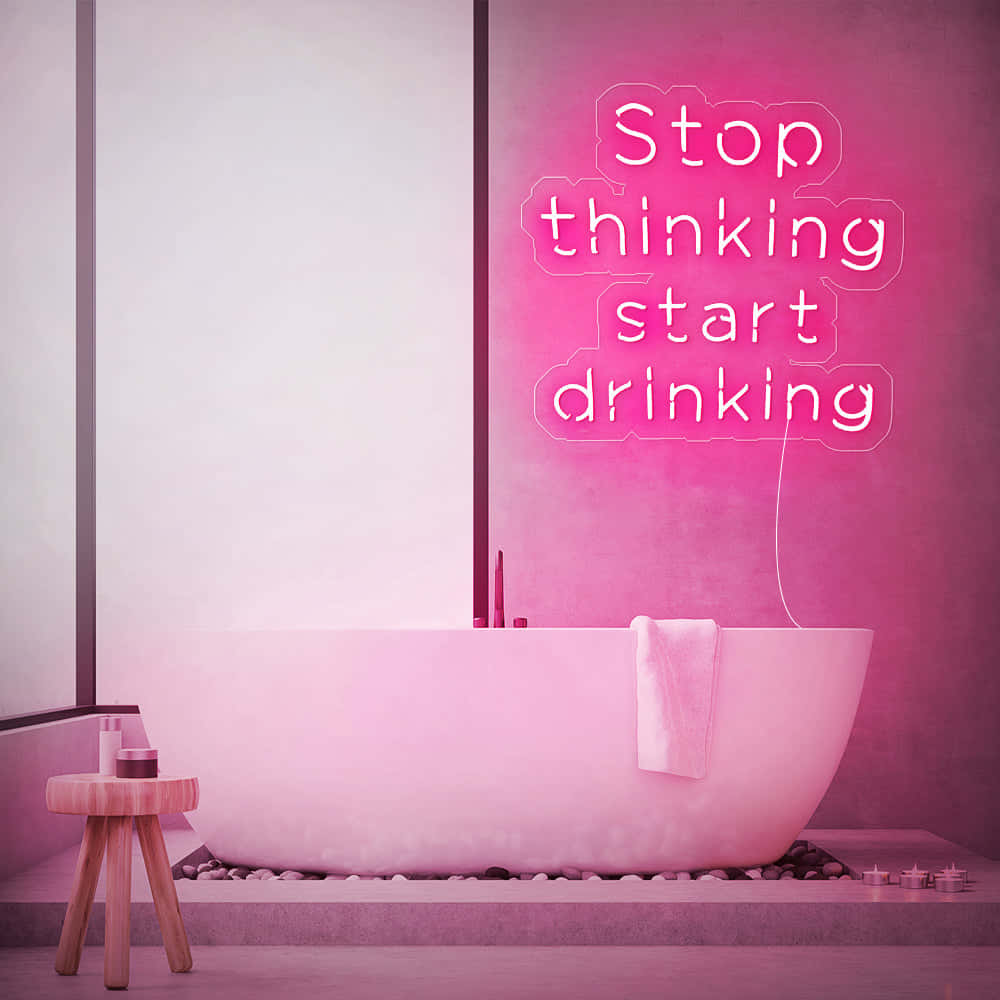 Aesthetic Grunge Neon Signs 桌布 壁紙 — 一個現代浴室，被牆上寫著「Stop thinking start drinking」的粉紅色霓虹燈牌照亮，燈牌位於獨立浴缸上方。