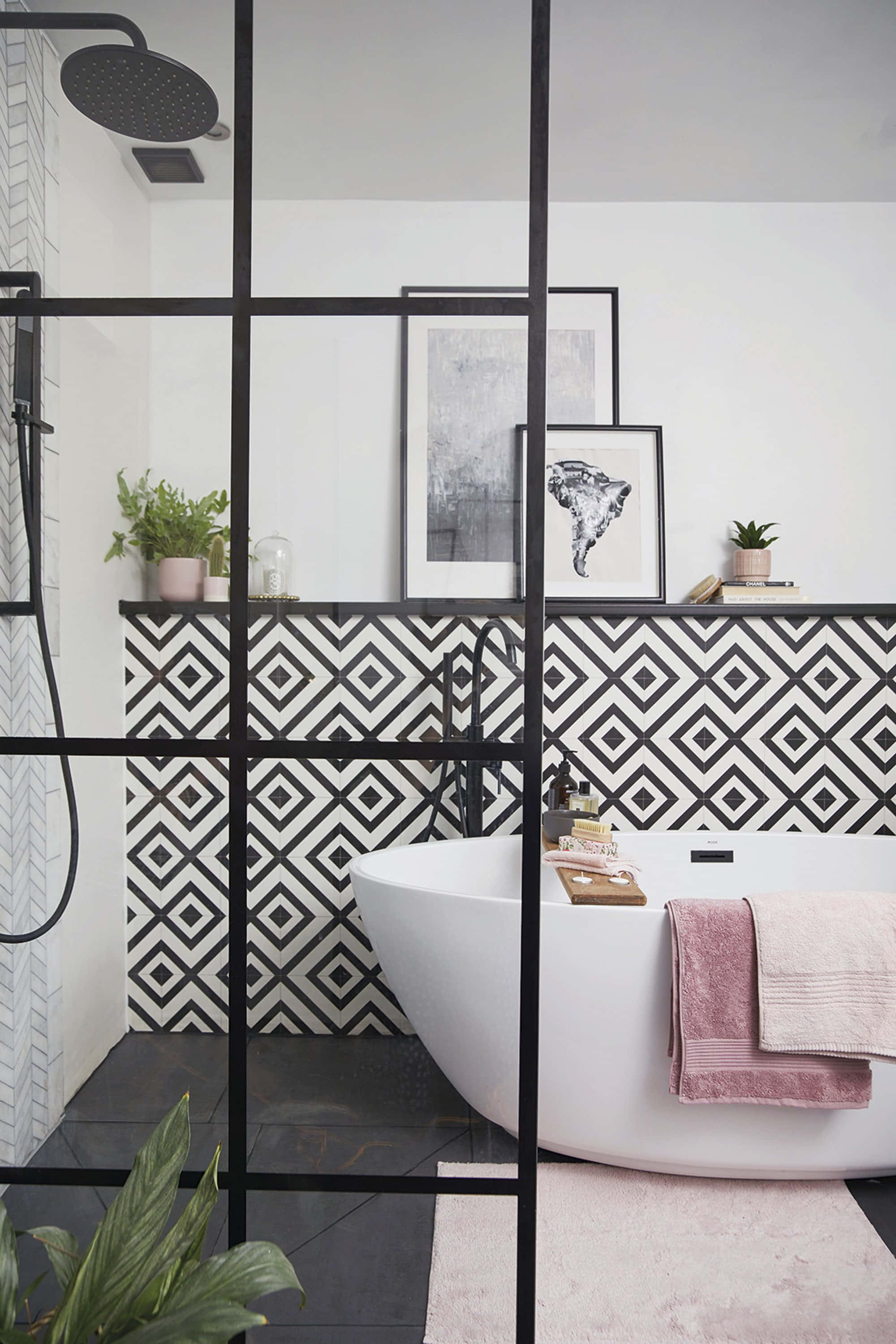 Bathroom Decor 桌布 壁紙 — 一個現代浴室，配有獨立式白色浴缸、黑色幾何瓷磚和粉紅色毛巾，透過黑色格柵淋浴間觀看。