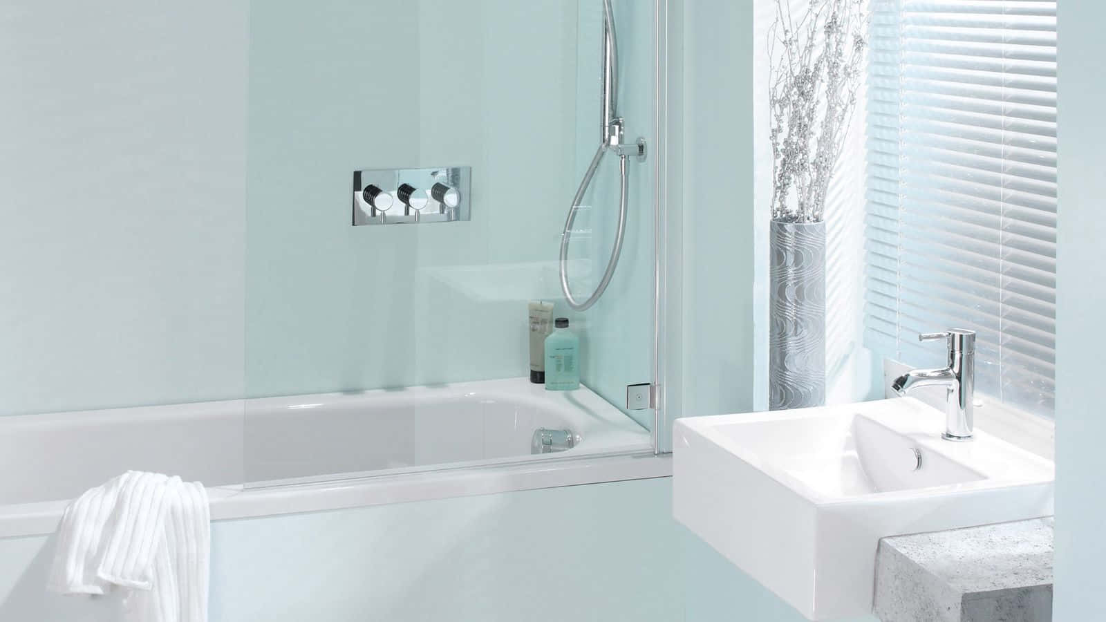 Bathroom Decor 桌布 壁紙 — 一個現代浴室，配有玻璃圍封的浴缸、白色洗手盆和柔和藍色牆壁，沐浴在自然光中。