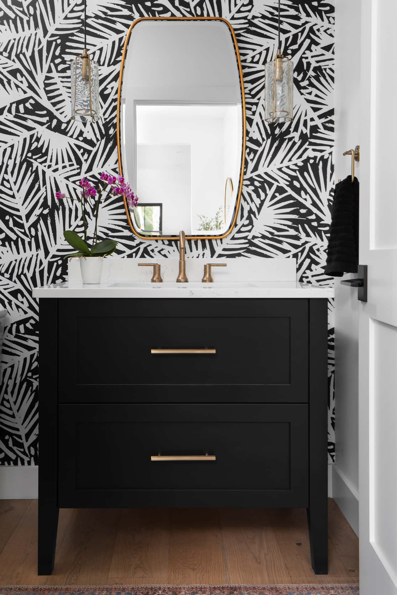 Black And White Bathroom 桌布 壁紙 — 一個現代浴室梳妝台，配有黑色抽屜、金色把手和醒目的黑白葉子圖案壁紙。