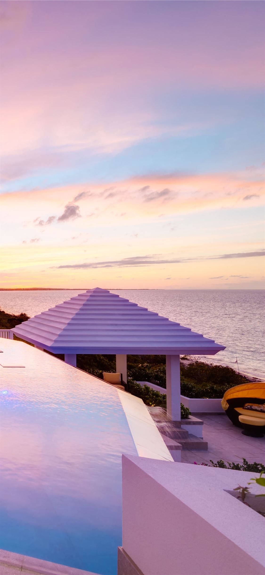 Turks And Caicos 桌布 壁紙 — 一個現代無邊際泳池俯瞰著寧靜的海洋，夕陽下呈現粉彩粉紅和橙色的天空。