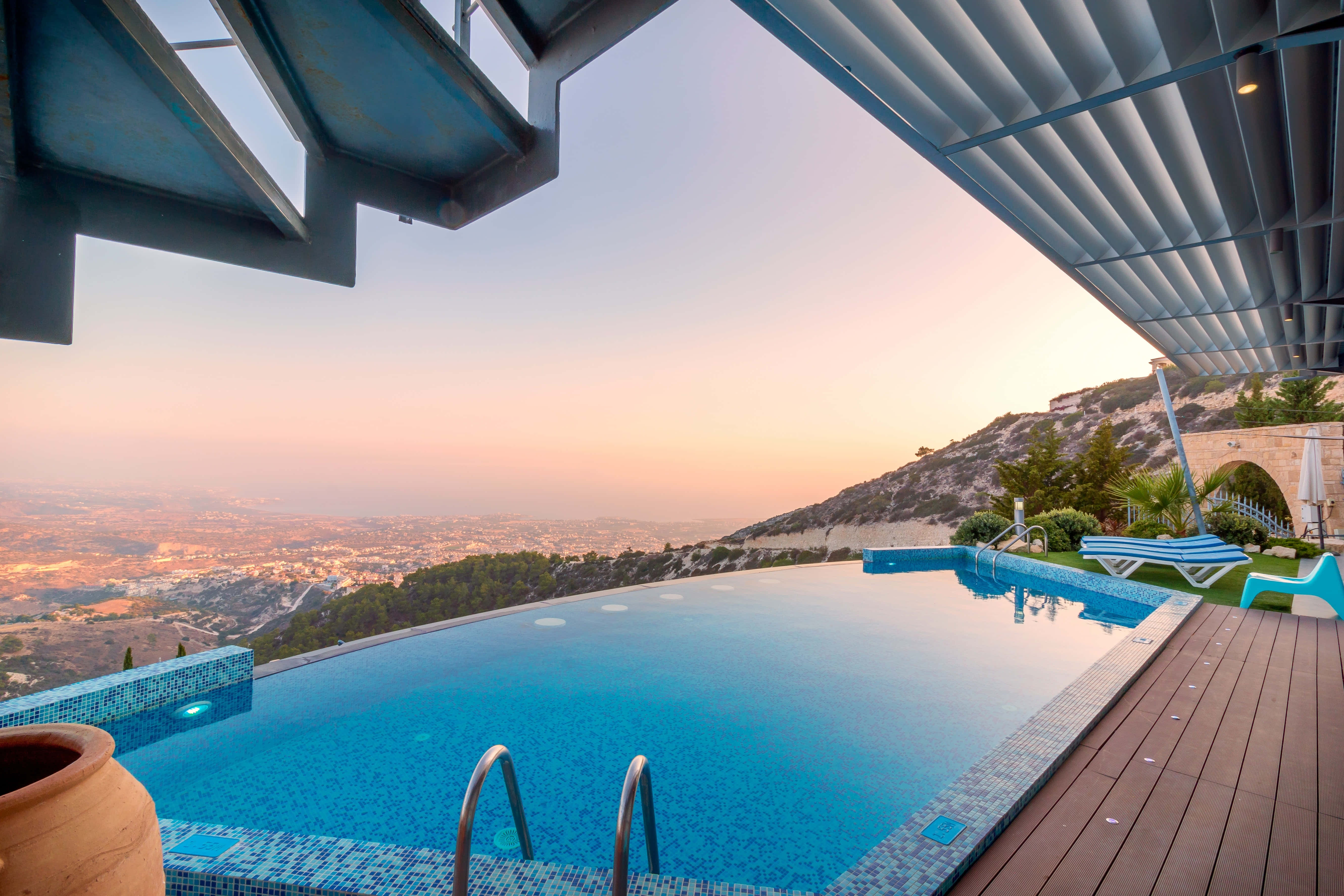 Swimming Pool 桌布 壁紙 — 一個現代無邊際泳池俯瞰著廣闊的山谷，夕陽西下時天空呈現溫暖的粉紅色和橙色。
