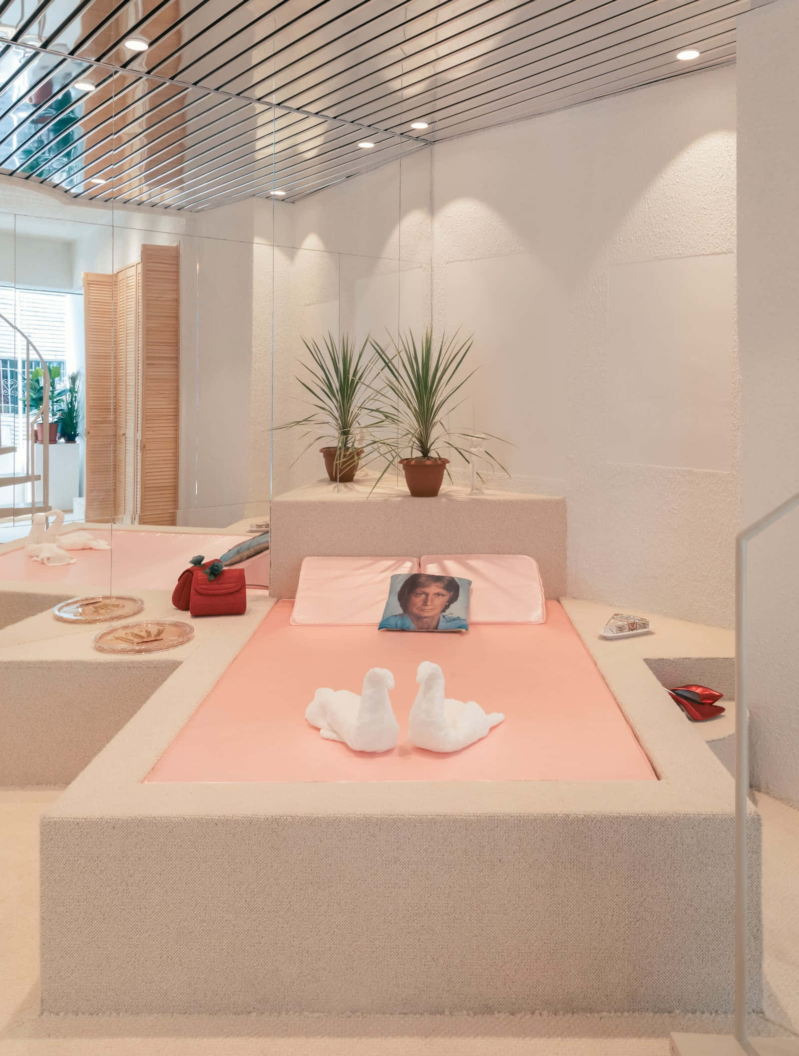 Interior Design 桌布 壁紙 — 一個現代簡約風格的臥室，配有嵌入式粉紅色床、毛巾天鵝、盆栽植物和鏡面牆，上方有明亮的吊燈。