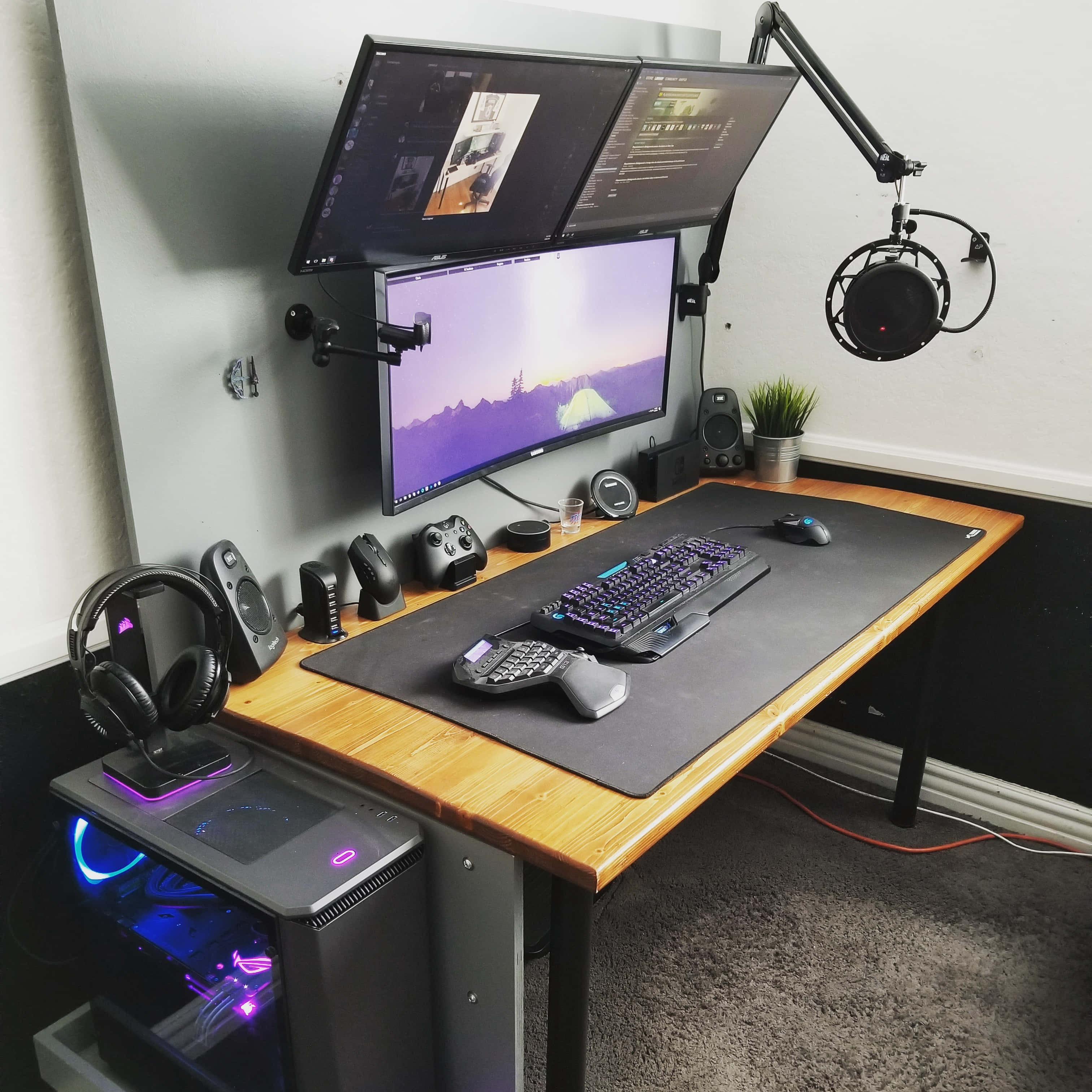 Gaming Pc Setup 桌布 壁紙 — 一個現代遊戲設置，配備三個顯示器、發光PC和木桌上的周邊設備。