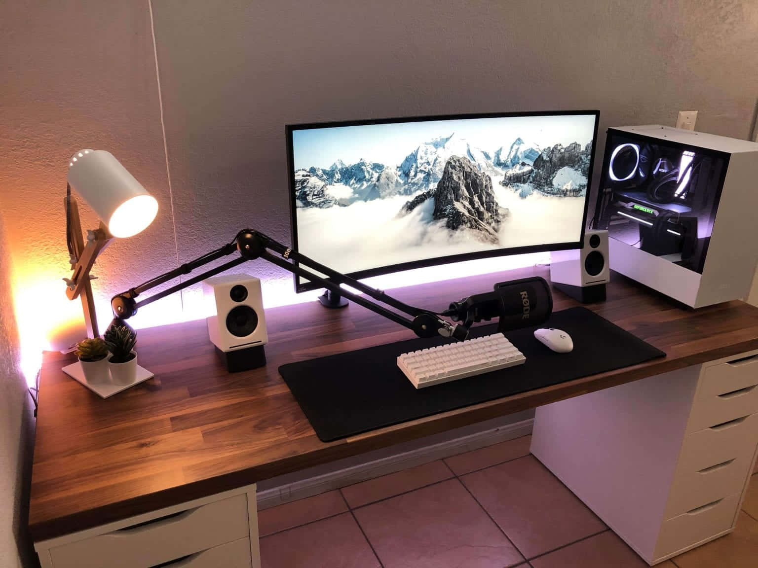 Gaming Pc Setup 桌布 壁紙 — 一個現代遊戲設置，配備曲面顯示器顯示雪山、白色鍵盤、RGB 燈光電腦和溫暖的檯燈。