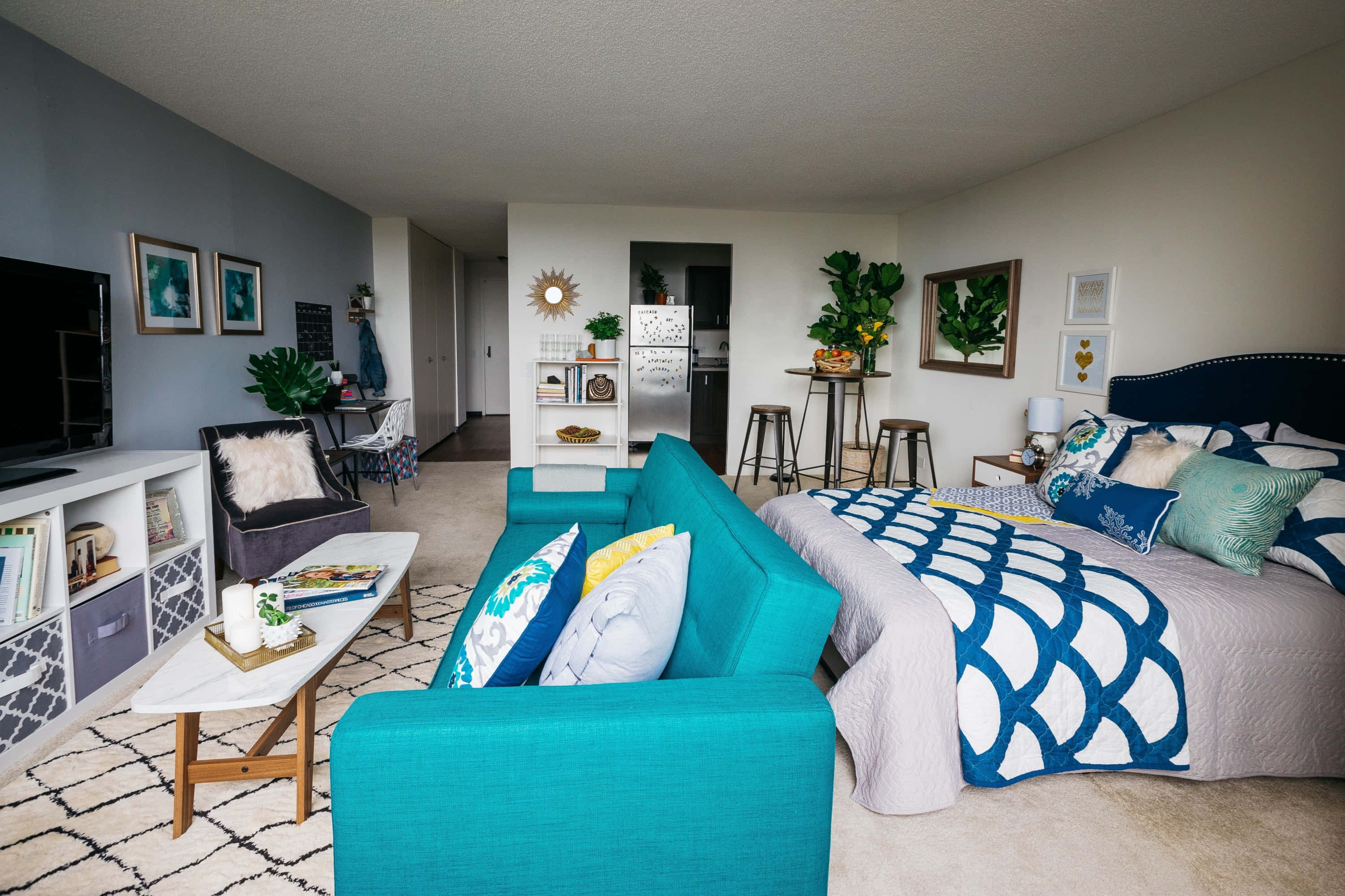 Apartment 桌布 壁紙 — 一個現代開放式概念的臥室和起居區，設有鮮明的青綠色沙發、圖案床上用品和海岸裝飾，在明亮的日光下。