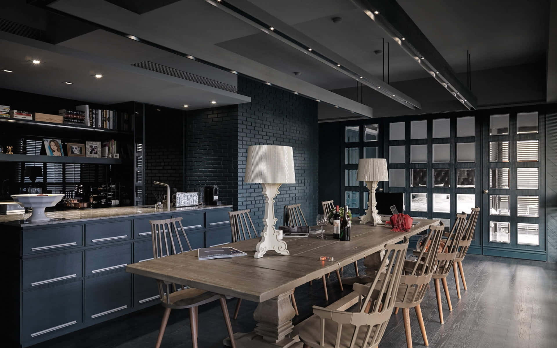 Dining Room 桌布 壁紙 — 一個現代飯廳，設有長木桌，周圍擺放淺色木椅，搭配深藍色櫥櫃和磚牆，天花裝有工業風吊燈。