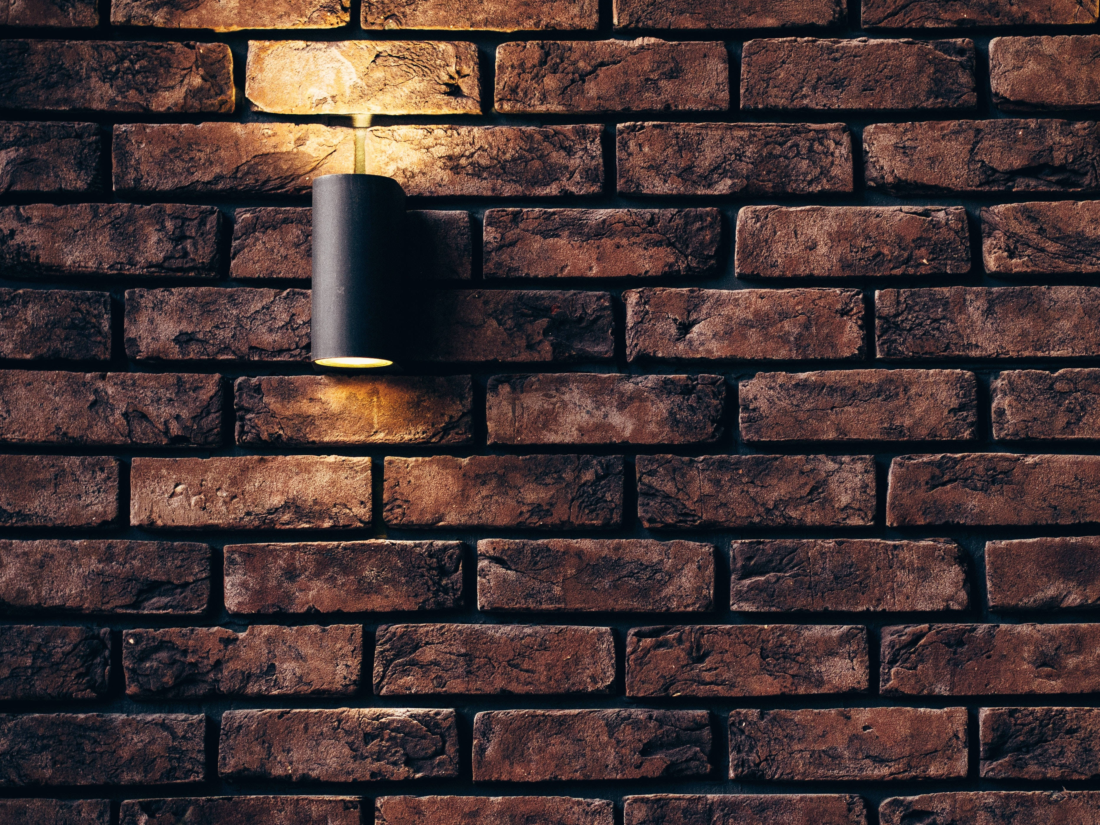 Brick 桌布 壁紙 — 一個現代黑色壁燈在夜間將溫暖的光線投射在有紋理的質樸磚牆上。