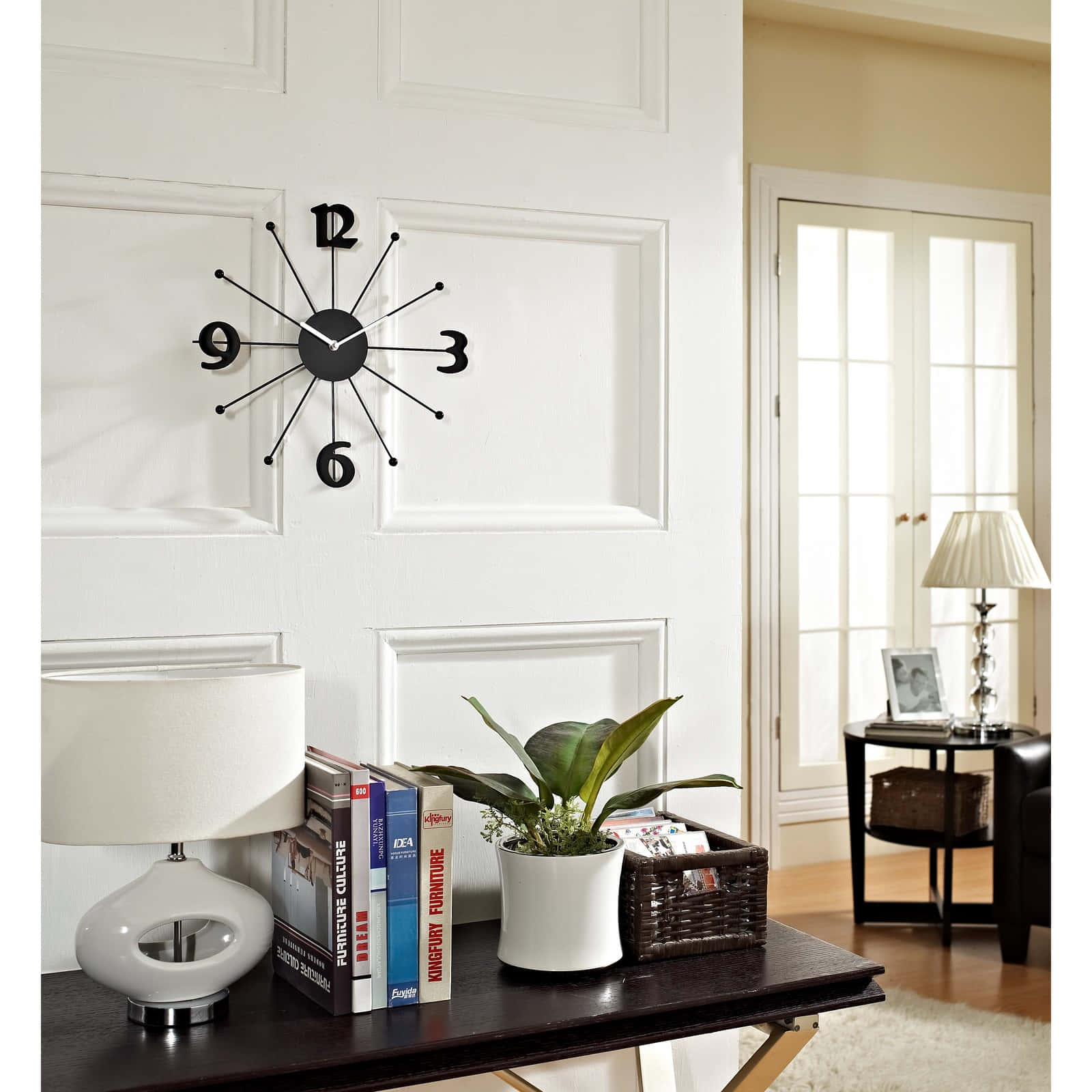 Wall Clock 桌布 壁紙 — 一個現代黑色星爆掛鐘掛在深色木質玄關桌上，桌上放著白色檯燈、書籍、盆栽植物和一個編織籃，位於明亮通風的客廳中。