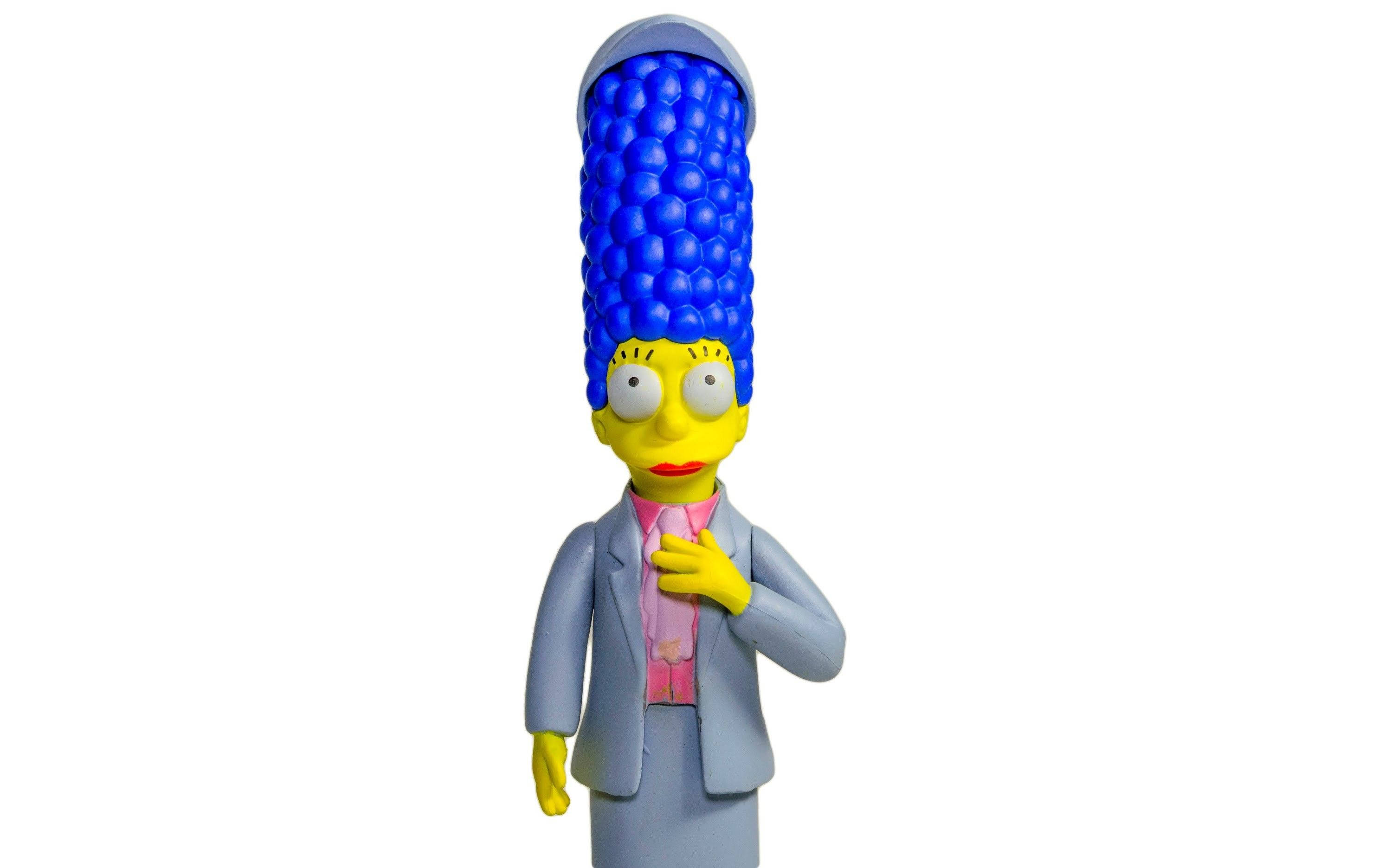 marge 桌布 壁紙 — 一個瑪姬·辛普森的公仔，擁有標誌性的藍色蜂窩頭，手放在胸前，背景為白色。